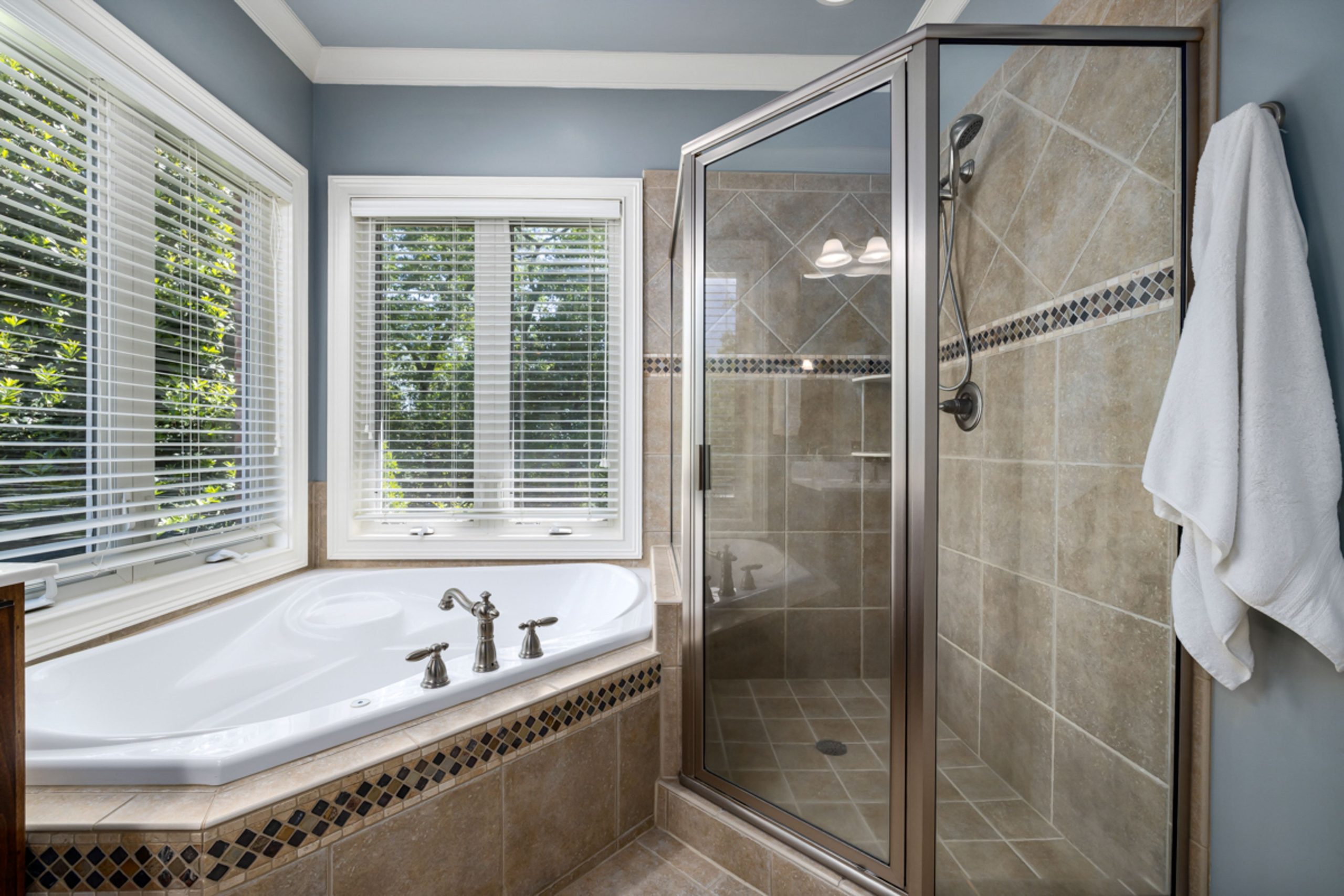 Elegant bathroom with glass shower, soaking tub, and large windows offering natural light.