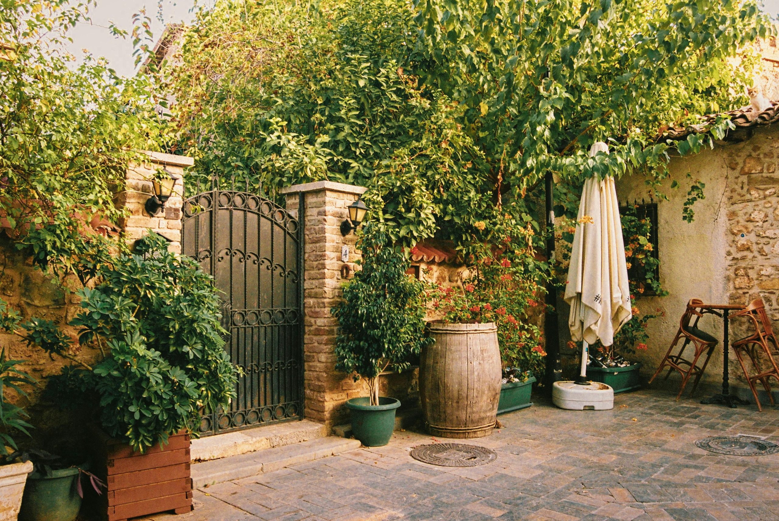 Elegant garden courtyard with lush greenery, stone brick accents, and a rustic metal gate.