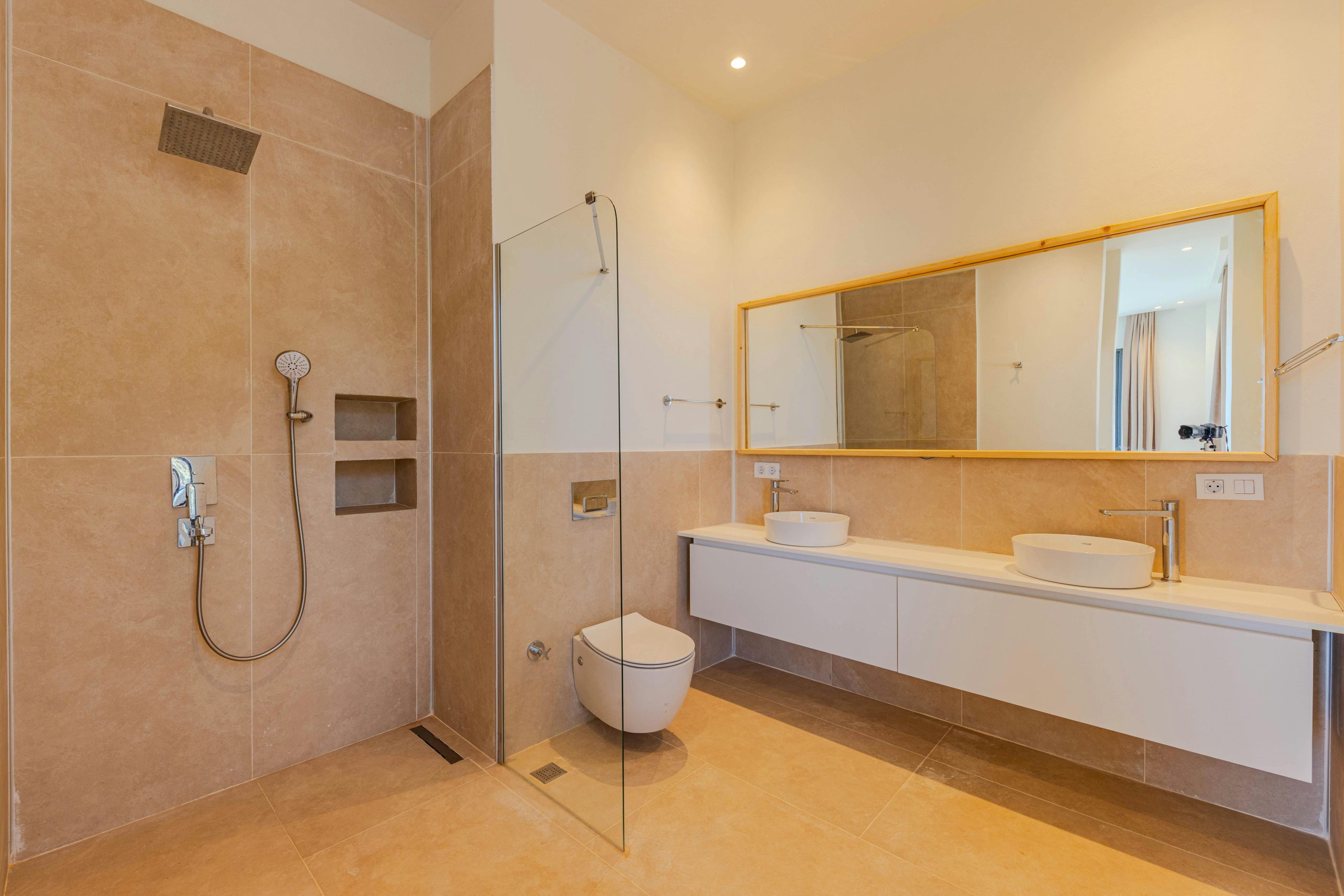 Elegant minimalist bathroom featuring beige tiles, large mirror, and double sinks.