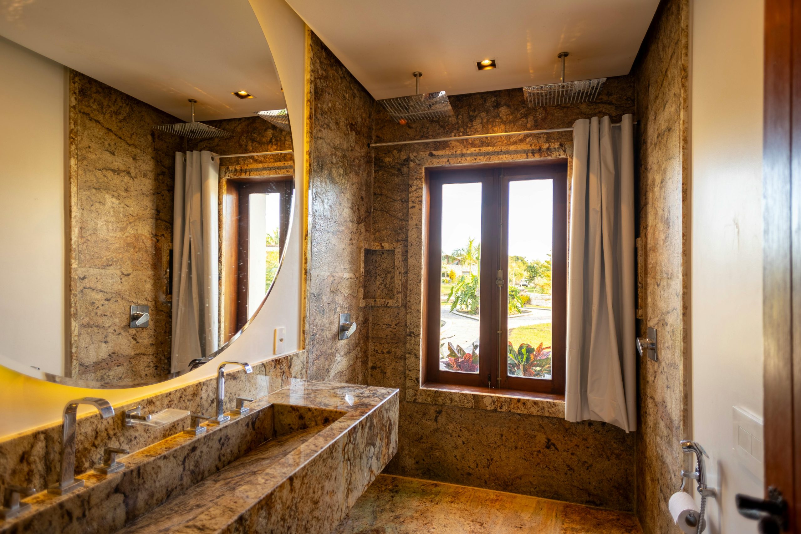 Elegant modern bathroom in Itaúnas, Brazil, featuring a stone finish, large mirror, and natural light.