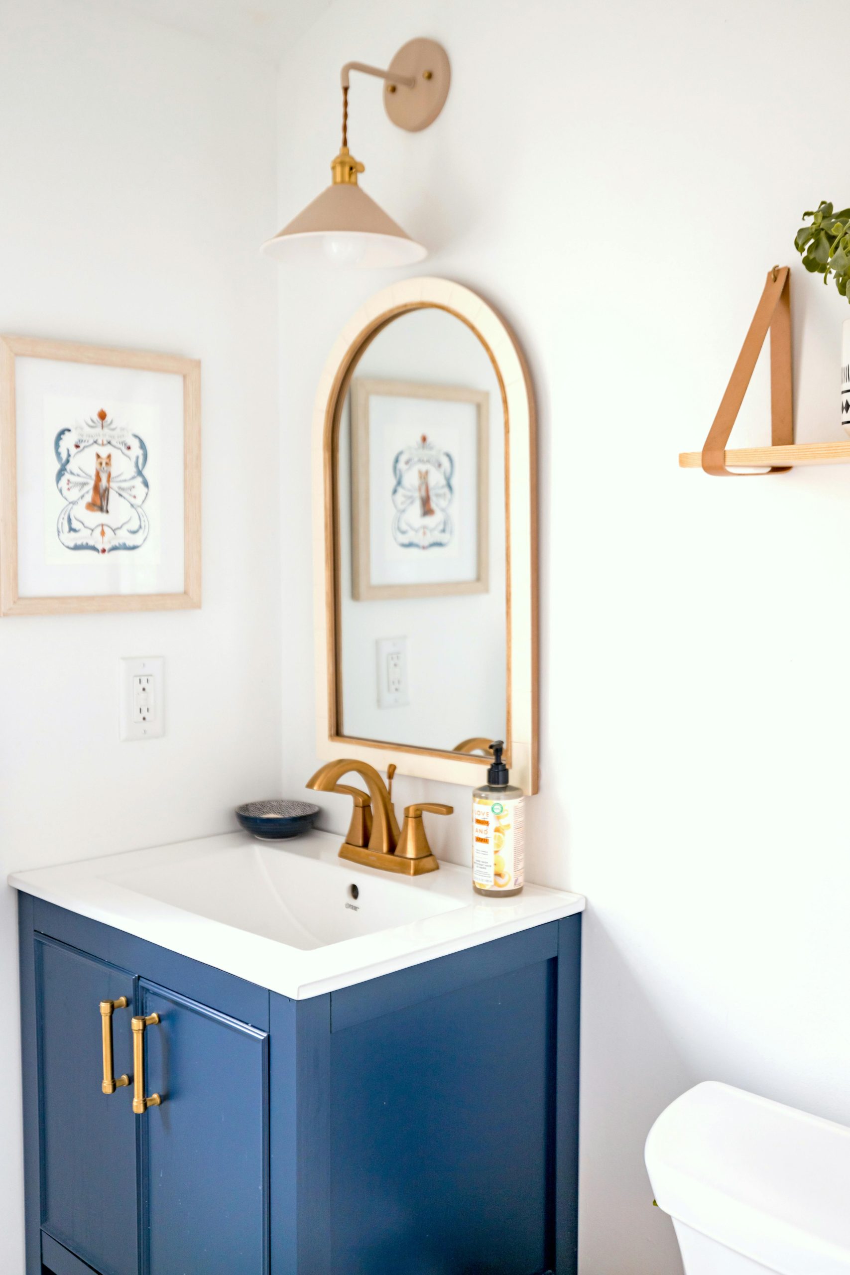 Elegant modern bathroom with navy cabinet, gold accents, and wall art.