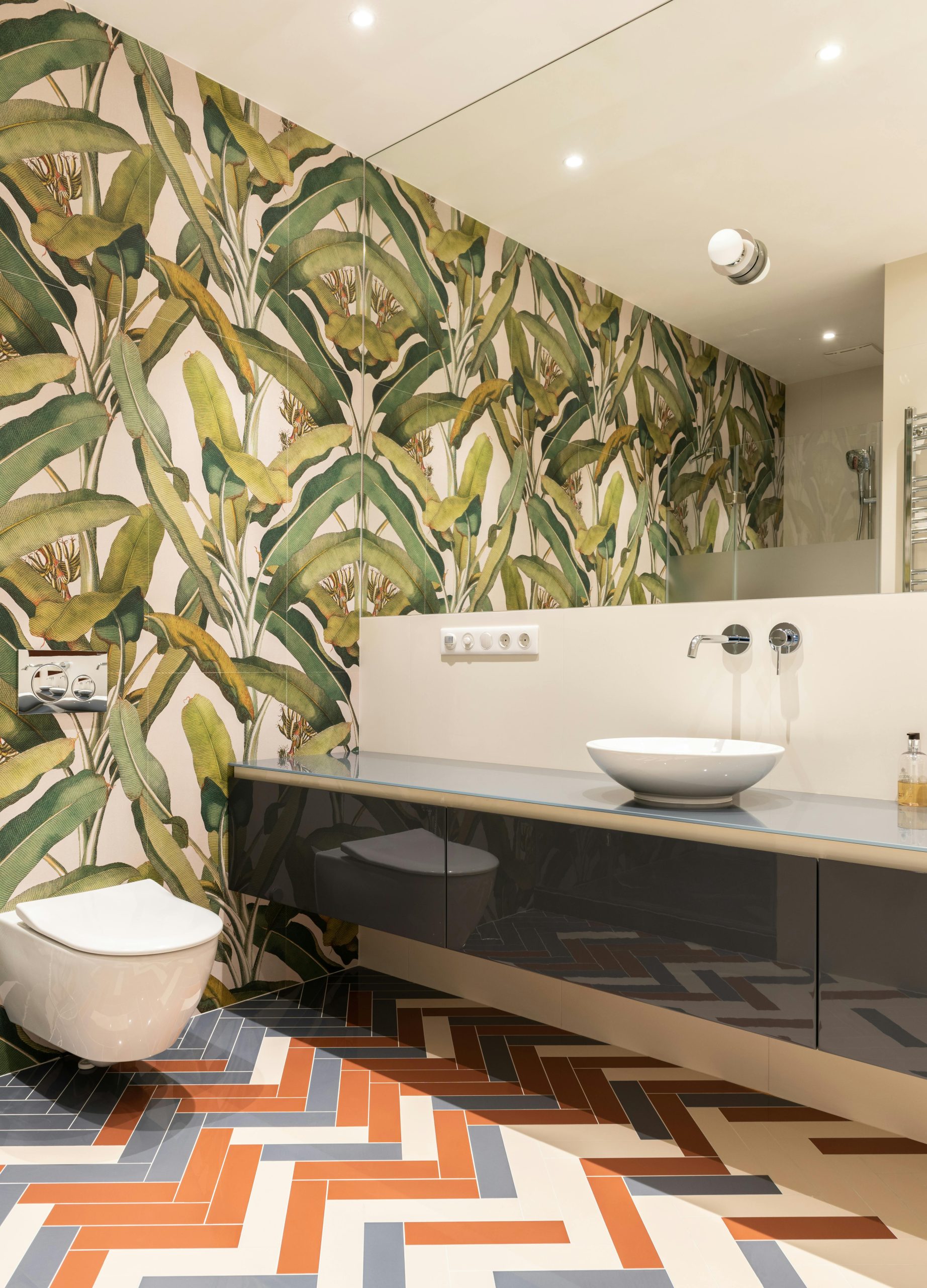 Interior of light bathroom with white toilet near sink on cabinet near mirror and colorful walls and floor