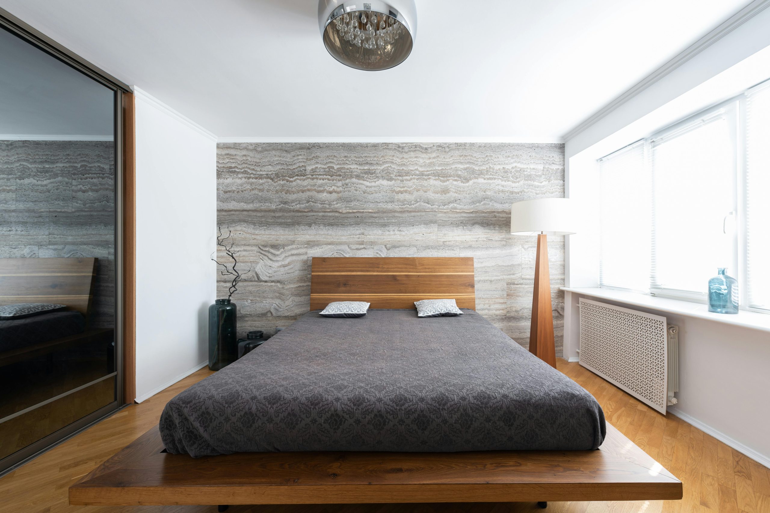 Interior of light modern flat with bed near lamps on floor and ceiling near vases with leafless sprig near mirror wall and window with windowsill