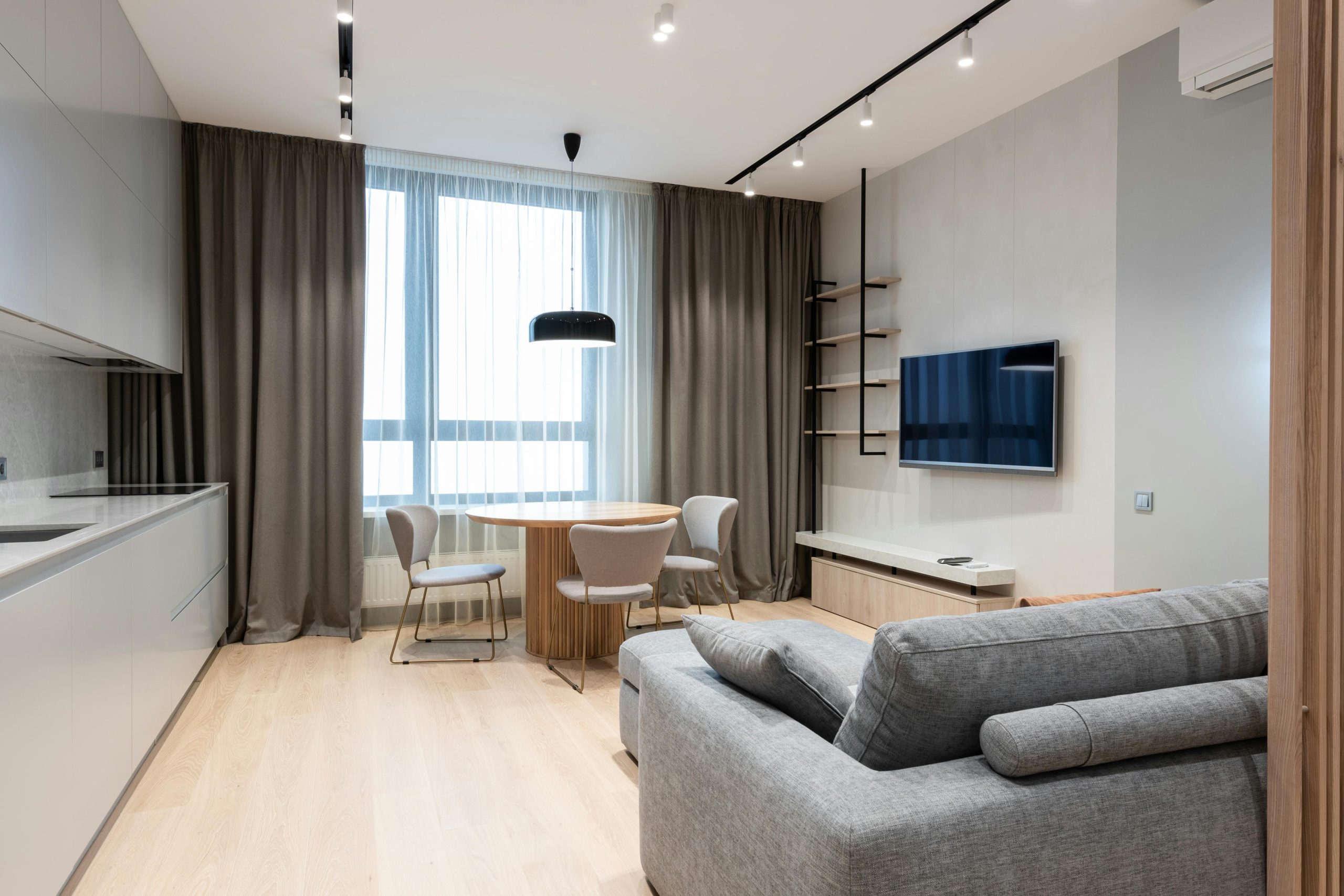 Interior of modern apartment with sofa in front of table with chairs and open kitchen next to TV on wall and window with curtains