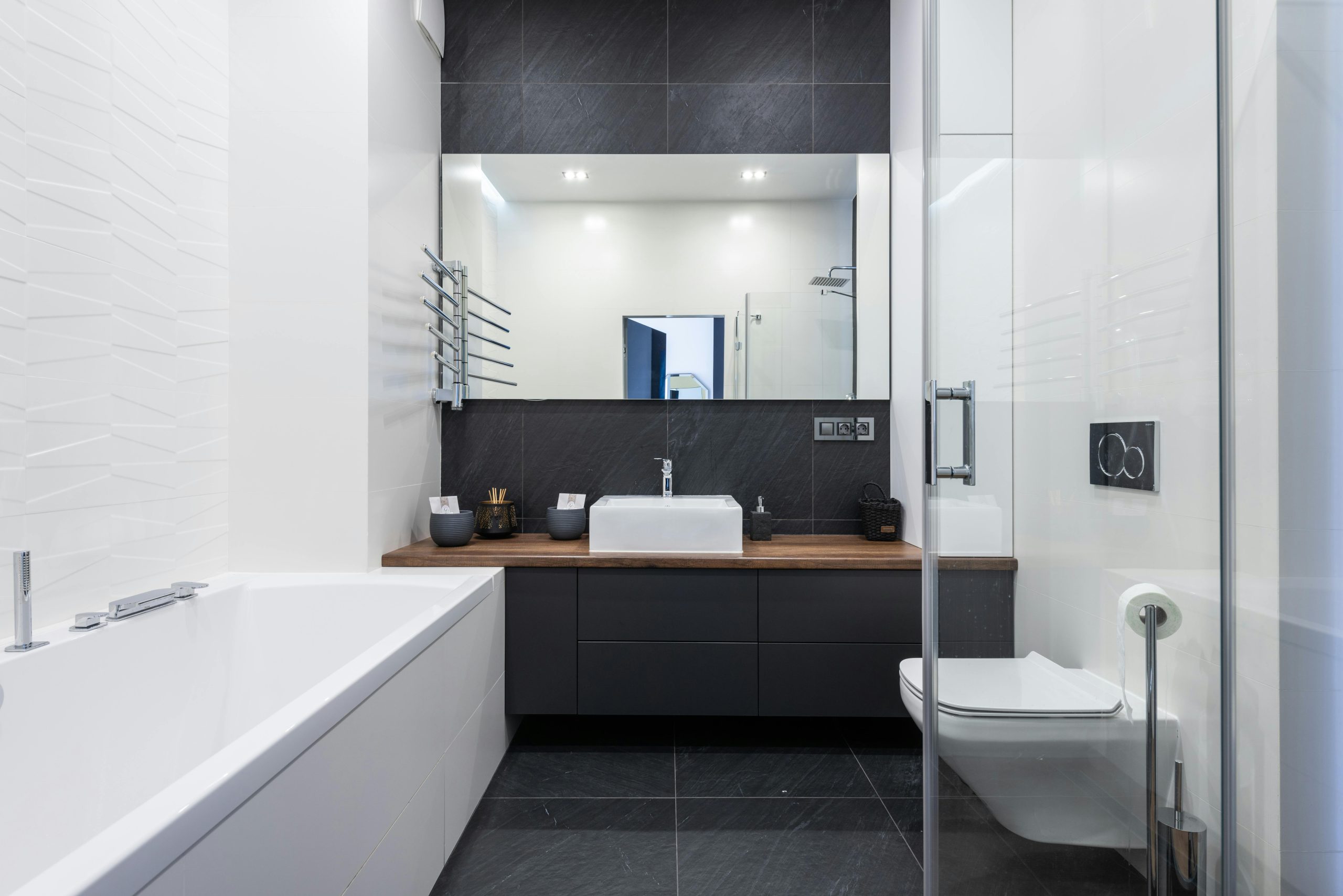 Interior of modern bathroom with bathtub near transparent shower cabin and toilet placed near black cupboard with sink and mirror