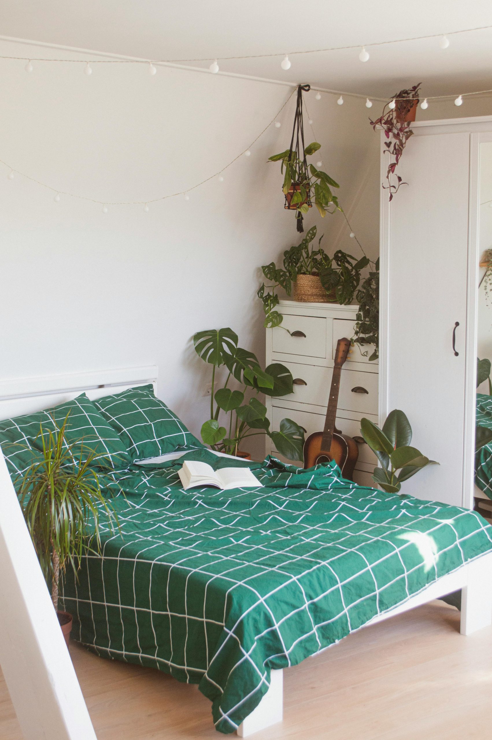 Inviting bedroom with green bedding, houseplants, and a guitar for a tranquil vibe.