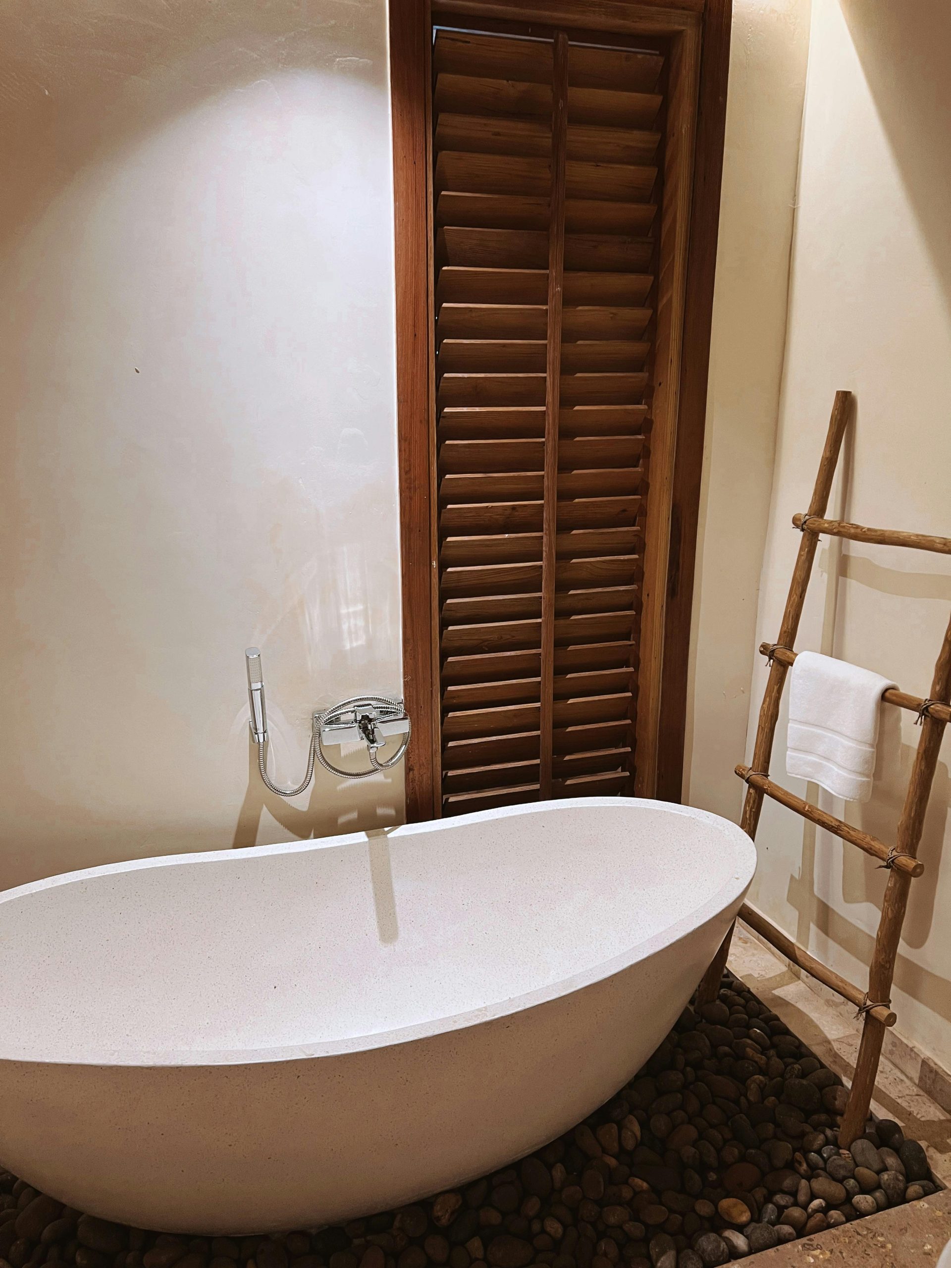 Minimalist bathroom featuring a stone-laden freestanding tub and wooden shutters.