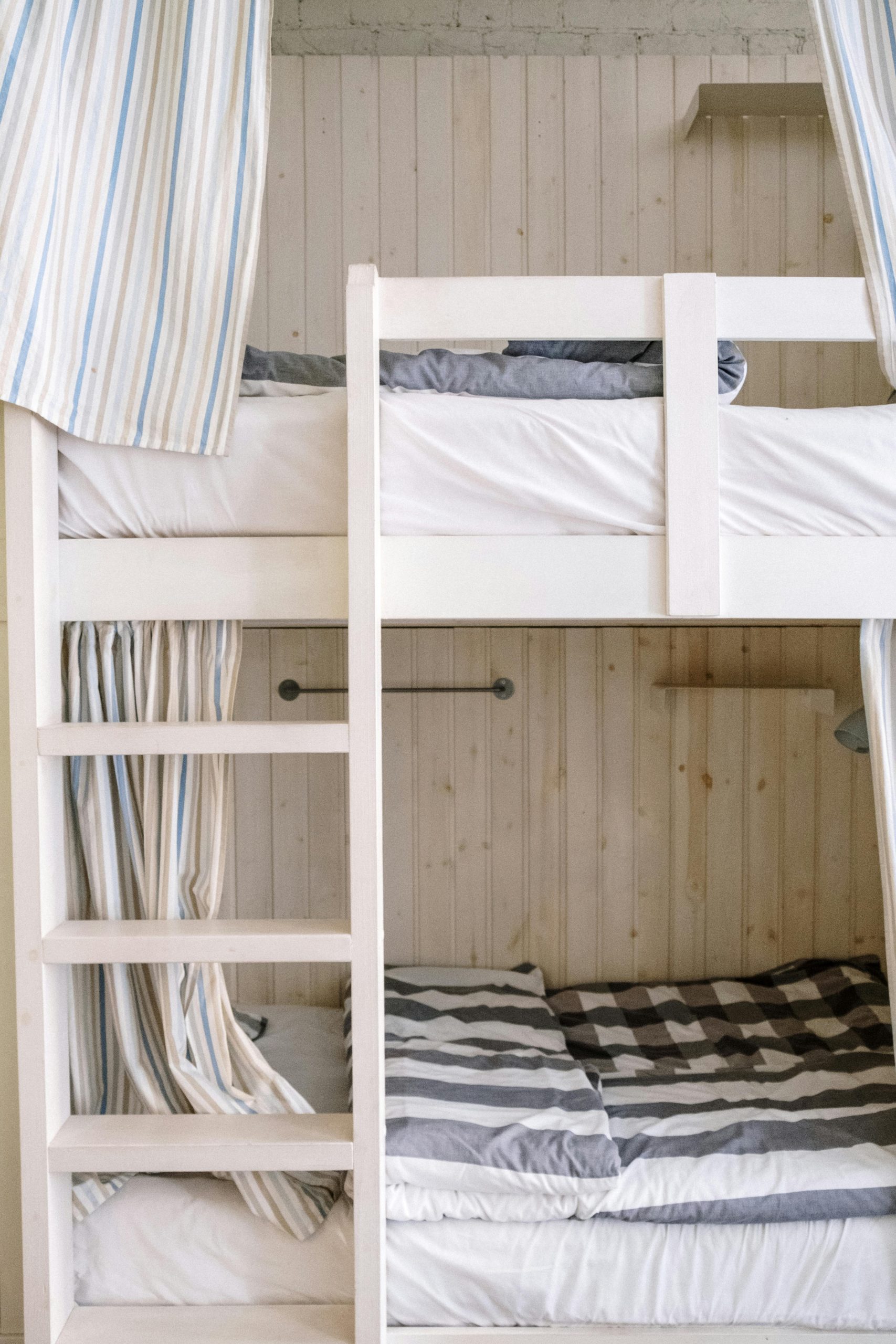 Minimalist bunk bed with striped bedding in a cozy, wooden-walled bedroom setting.