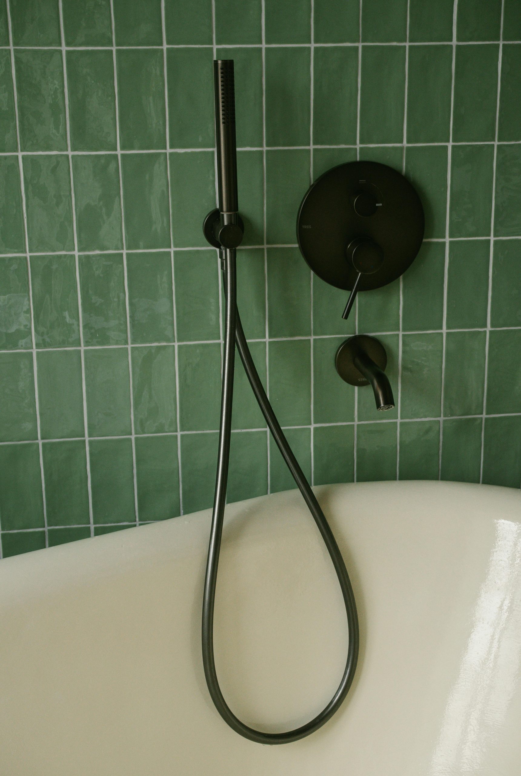 Modern bathroom featuring green tiles, a clean bathtub, and sleek black fixtures.