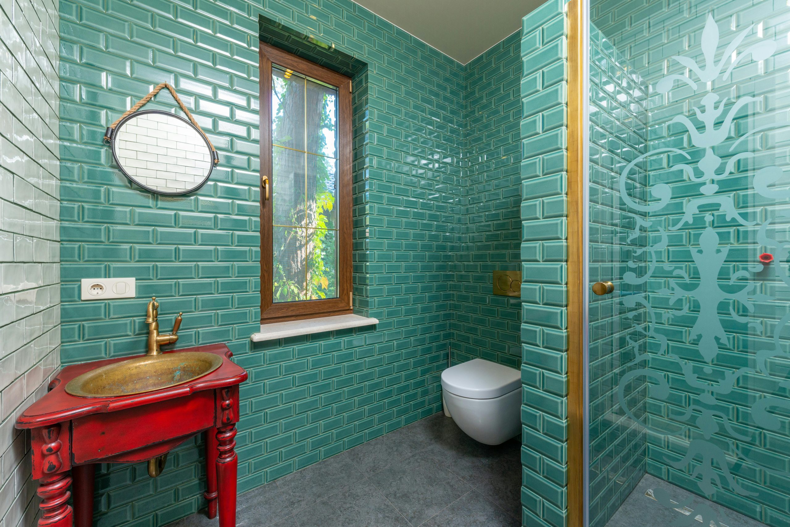 Modern bathroom with green tiled walls, gold fixtures, and elegant decor.