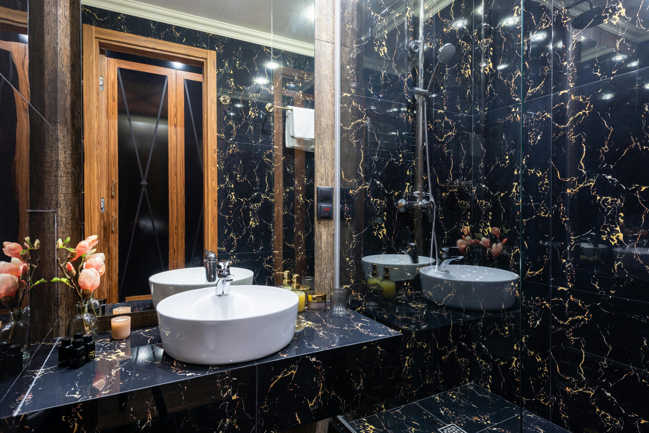 Modern bathroom with oval shaped washbasin between decorative flowers and toiletry product reflecting in mirror against door
