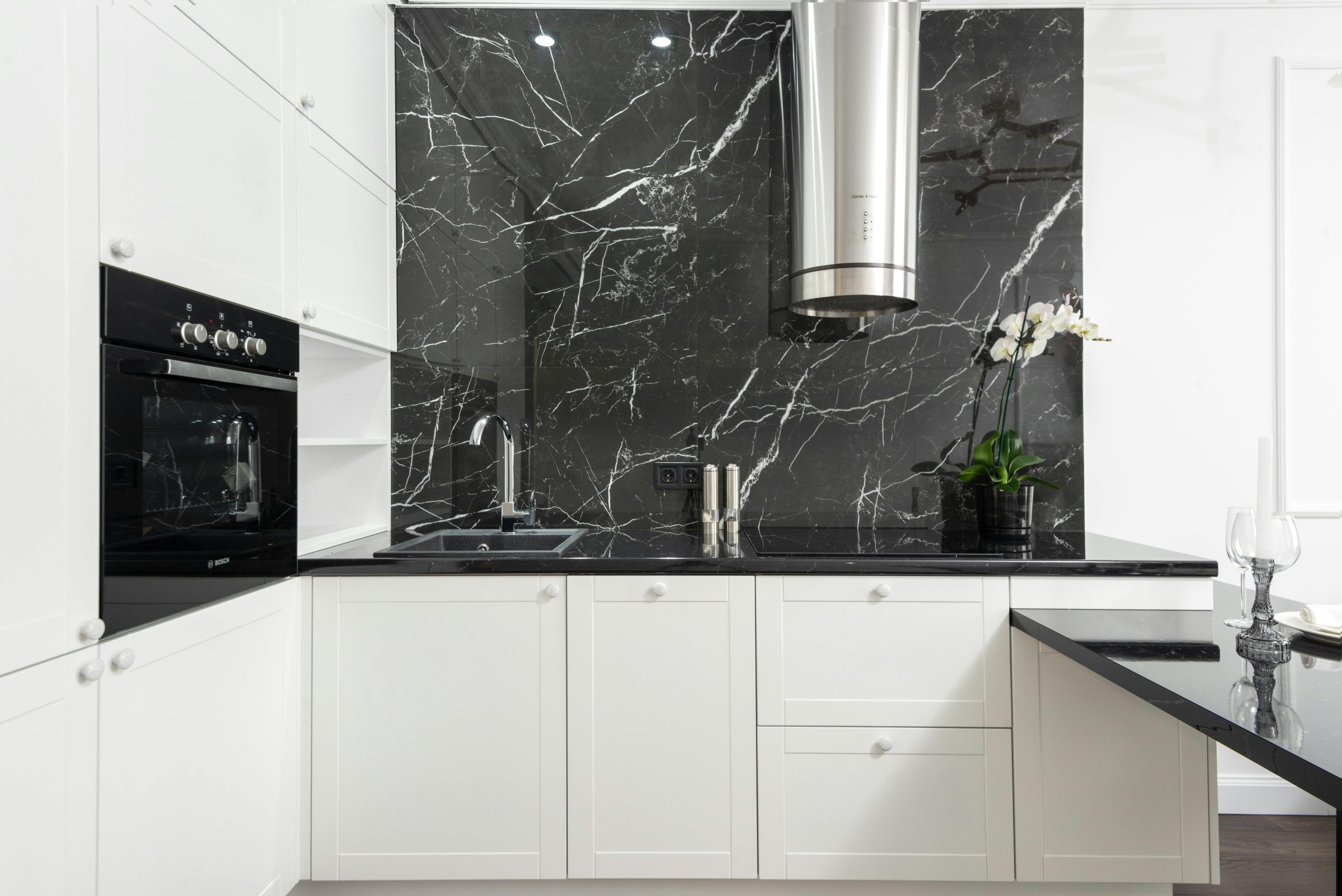 Sleek contemporary kitchen featuring white cabinets and black marble backsplash for a clean, minimalistic design.