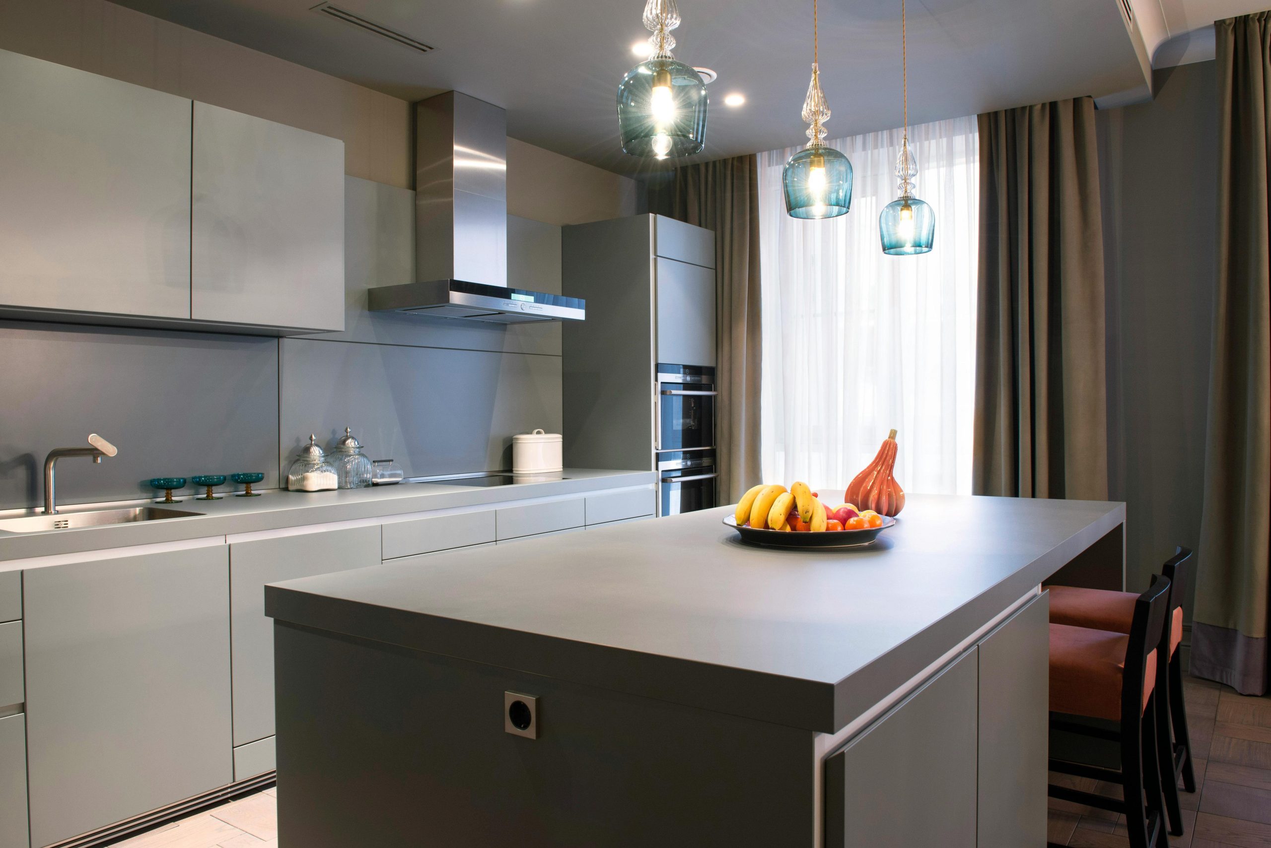 Sleek modern kitchen interior featuring a large island, elegant pendant lights, and fresh fruit decor.