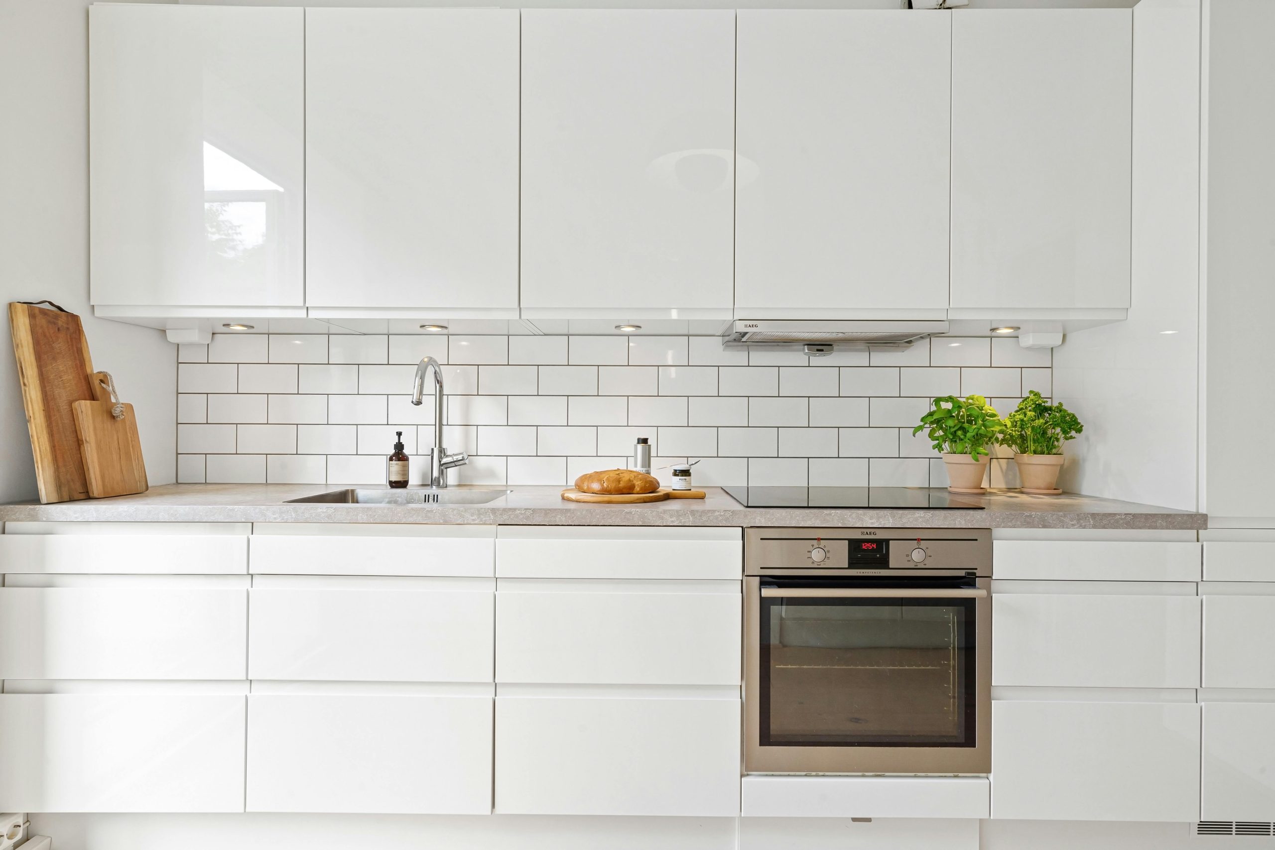 Sleek white kitchen featuring subway tiles, built-in oven, herbs, and bread for a modern touch.
