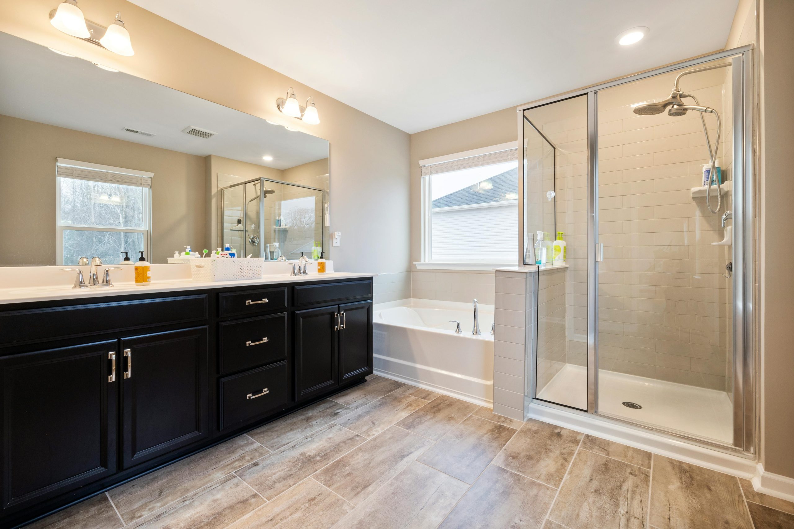 Spacious bathroom featuring a double vanity, bathtub, and glass-enclosed shower with natural light.