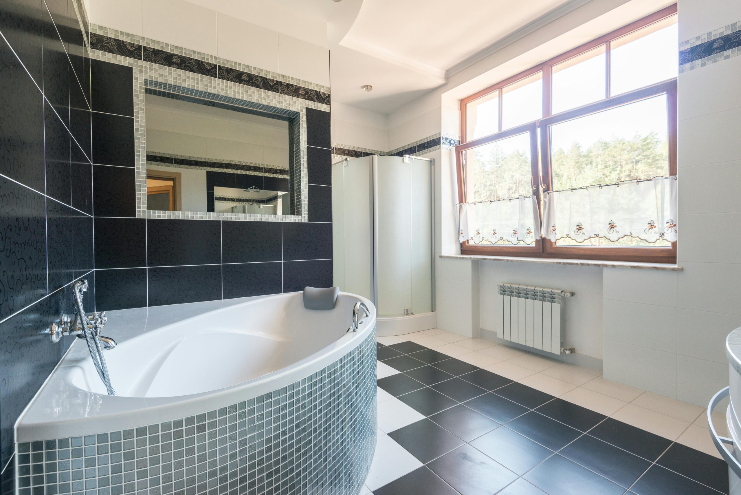 Spacious contemporary bathroom with a bathtub and large window, featuring black and white tiles.