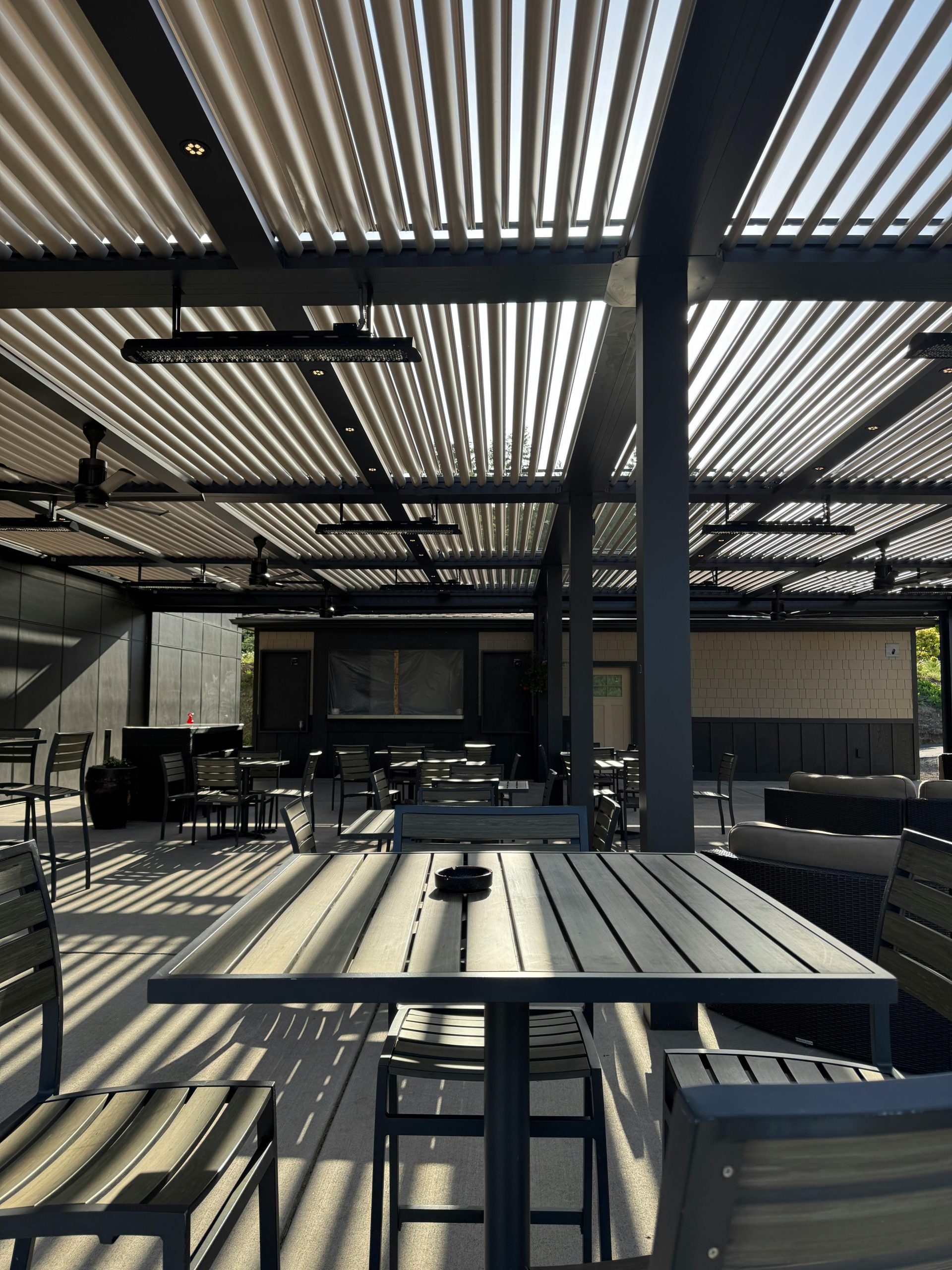 Stylish outdoor patio area with metal furniture and slatted pergola roof casting shadows, ideal for leisure.