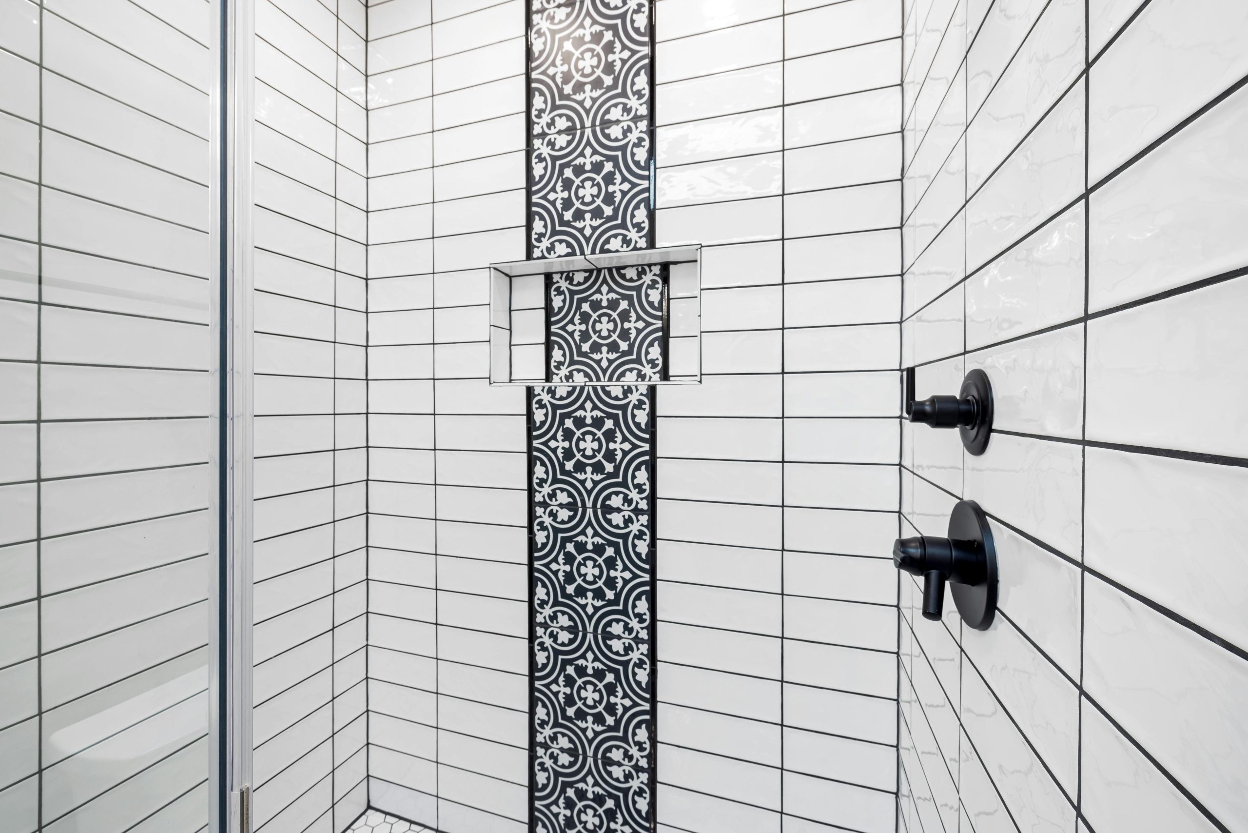 Stylish shower area featuring black and white geometric tiles and contemporary fixtures.