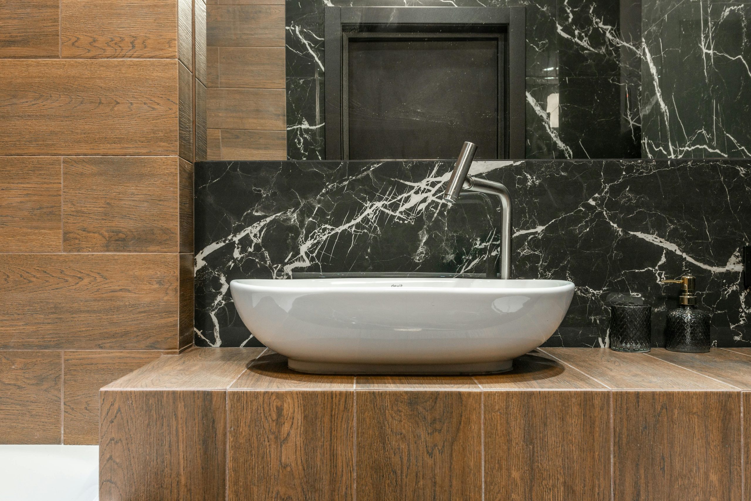 White sink and faucet in stylish modern bathroom with marble and wood look tiles