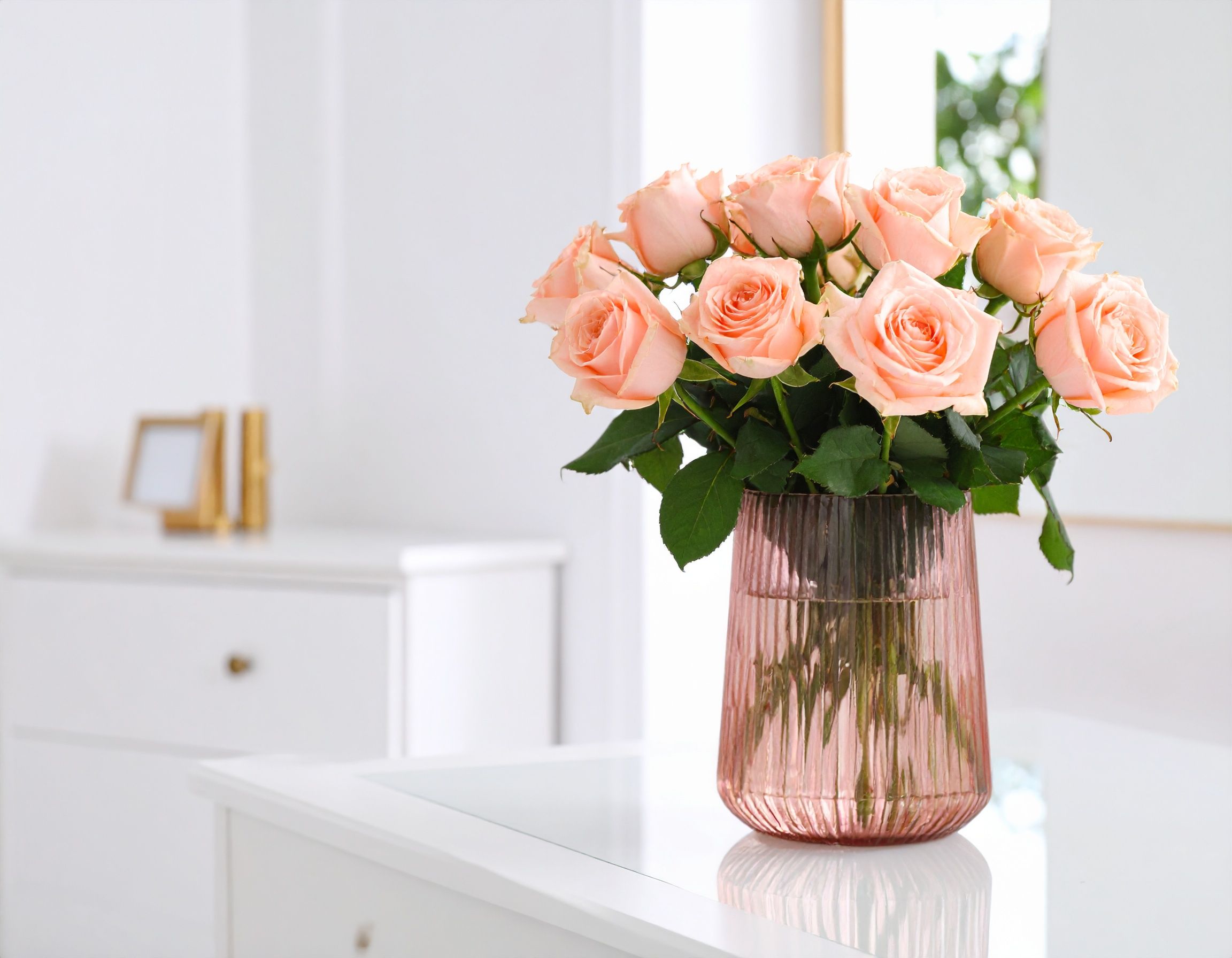 A bouquet of pink roses in a stylish glass vase on a white table, perfect for interior decor.