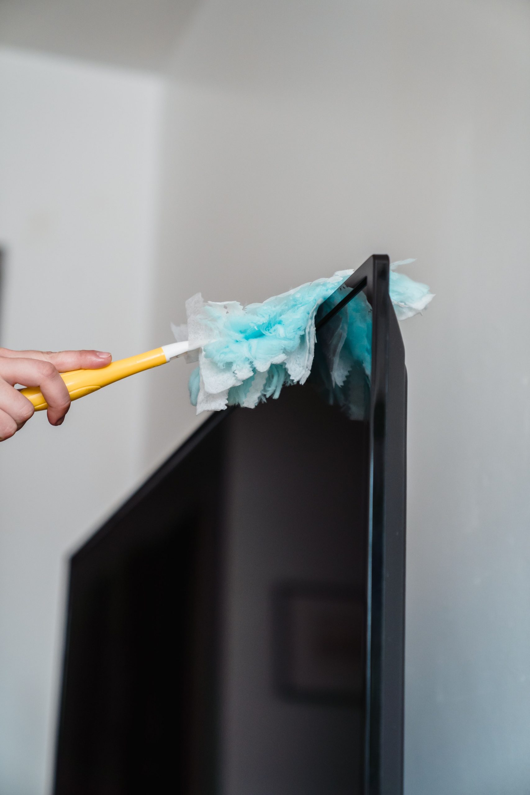 A close-up of cleaning a flat screen TV with a duster at home, showcasing housekeeping.