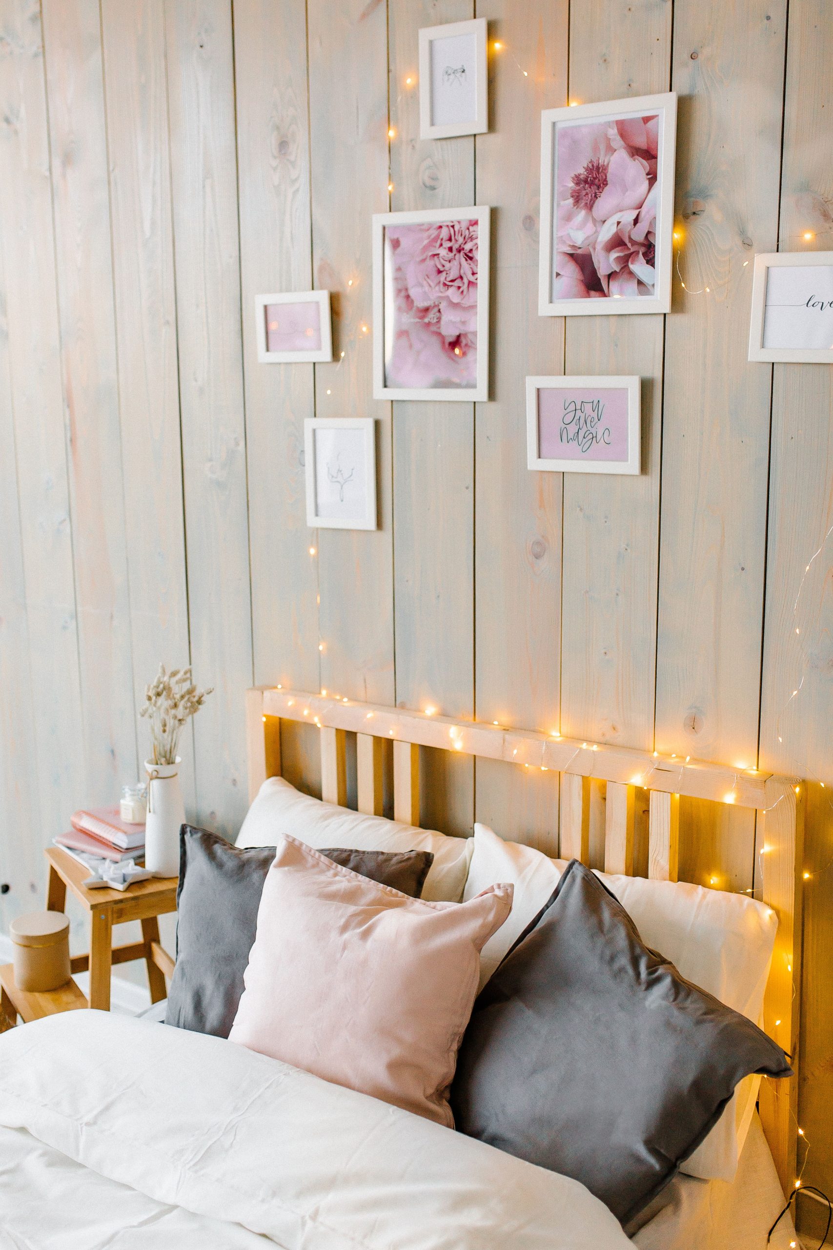 A cozy bedroom decorated with string lights and framed art on wooden walls.
