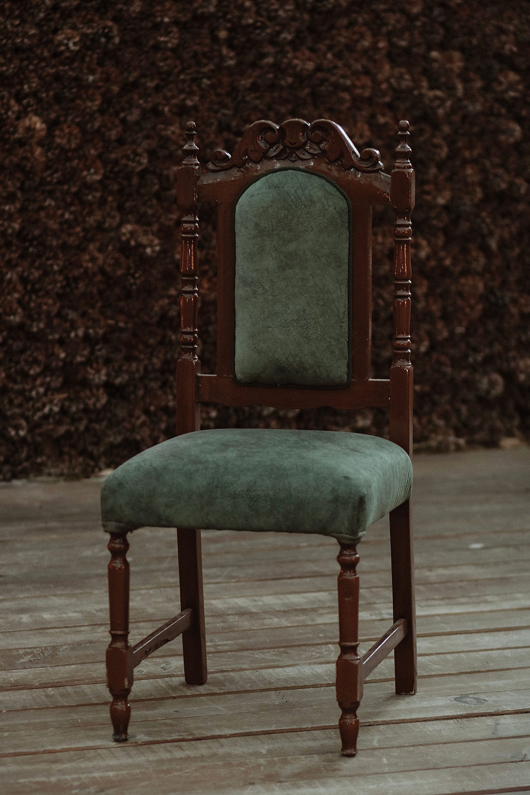 A green upholstered wooden chair with intricate carvings on an outdoor wooden deck.