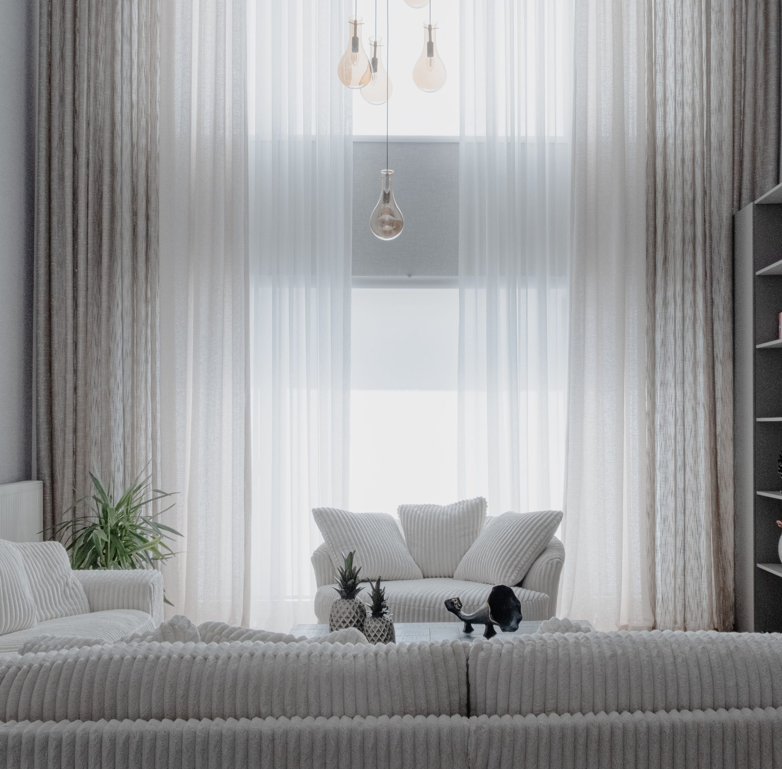 A minimalist living room with soft white sofas and large curtains, creating a cozy atmosphere.