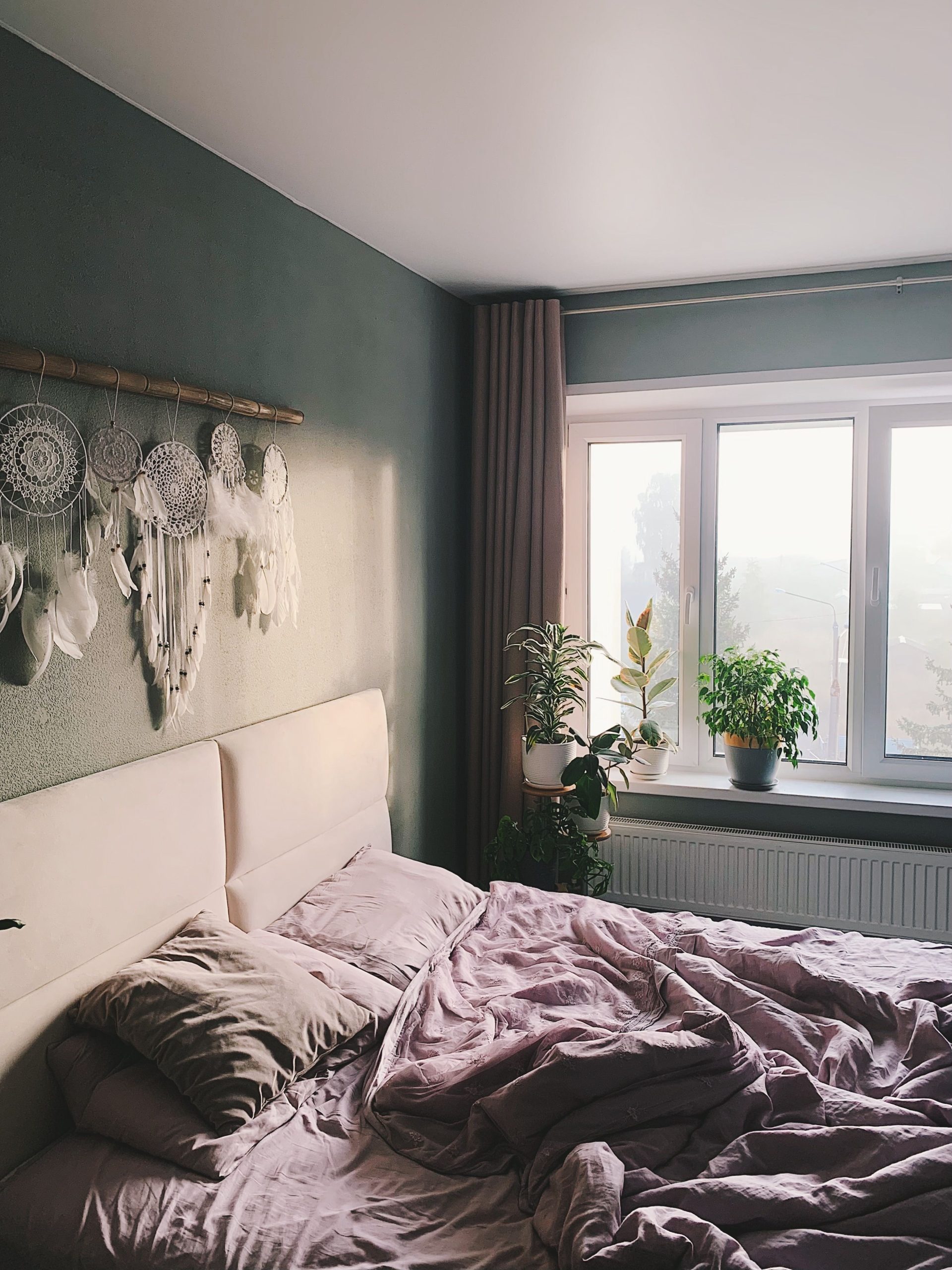 A modern, cozy bedroom featuring dreamcatchers and indoor plants.