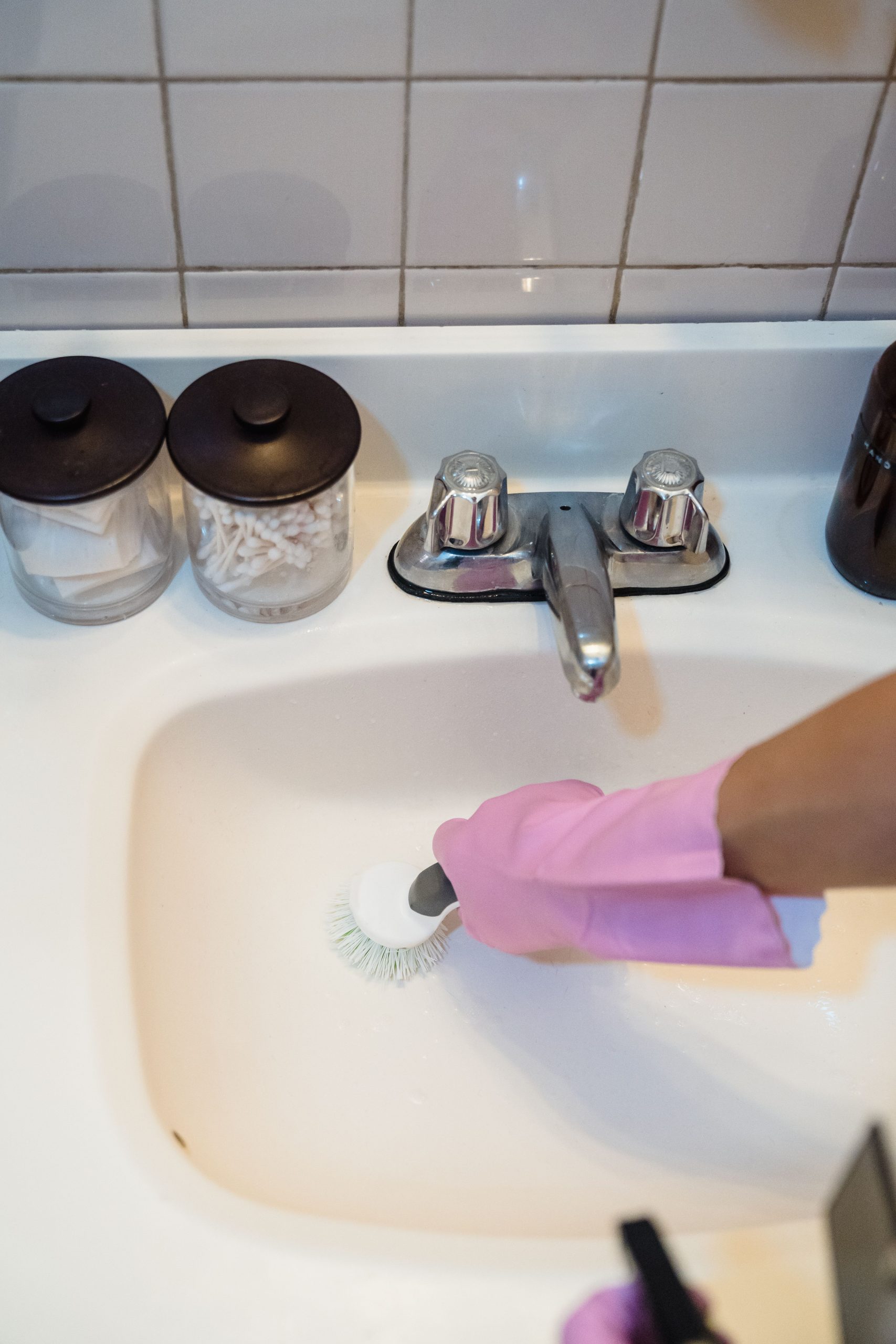 A person using a brush and pink gloves to clean a white bathroom sink, promoting hygiene and cleanliness.