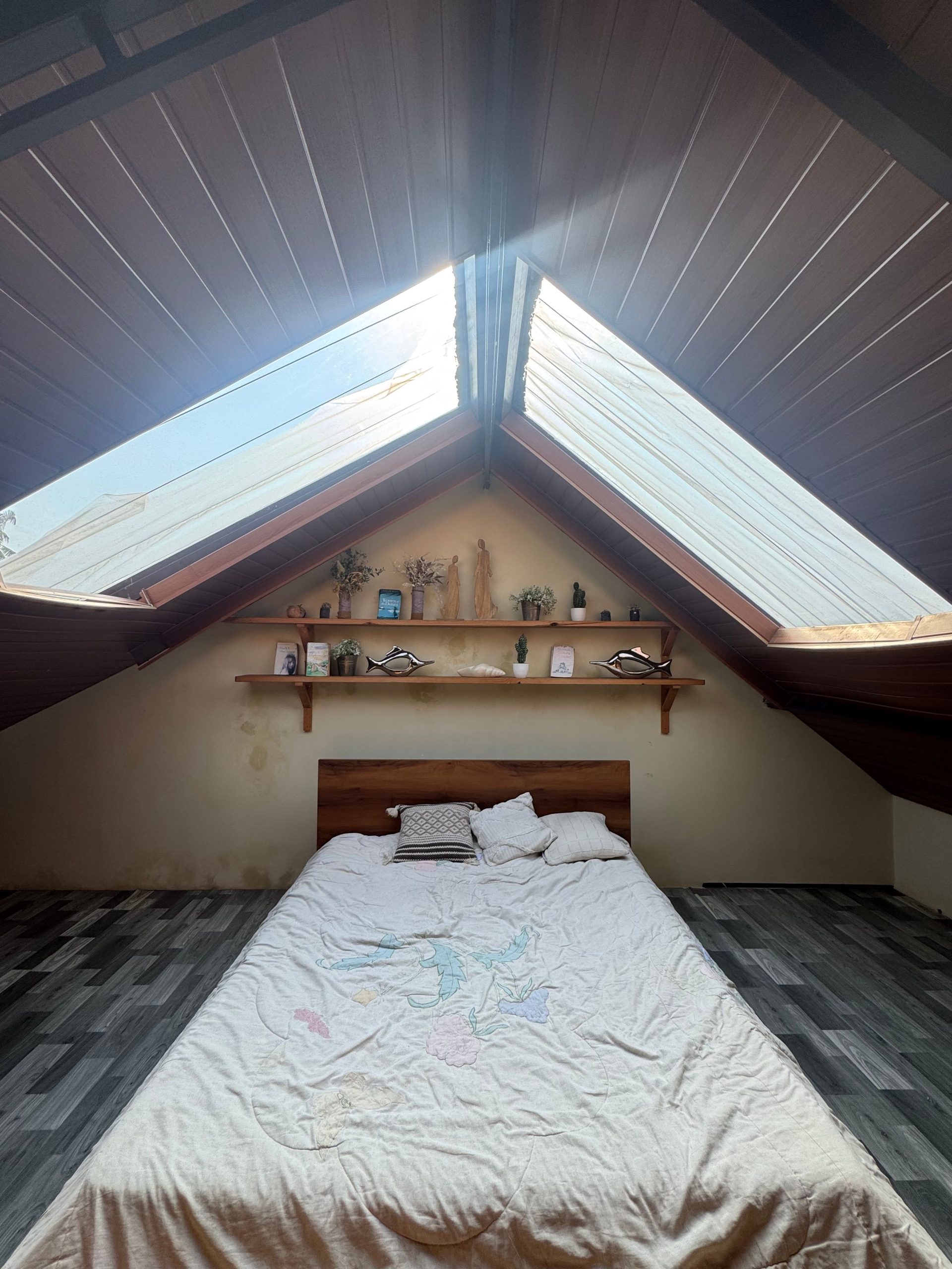 A serene loft bedroom featuring a double bed under large skylight windows, creating a bright and airy atmosphere.