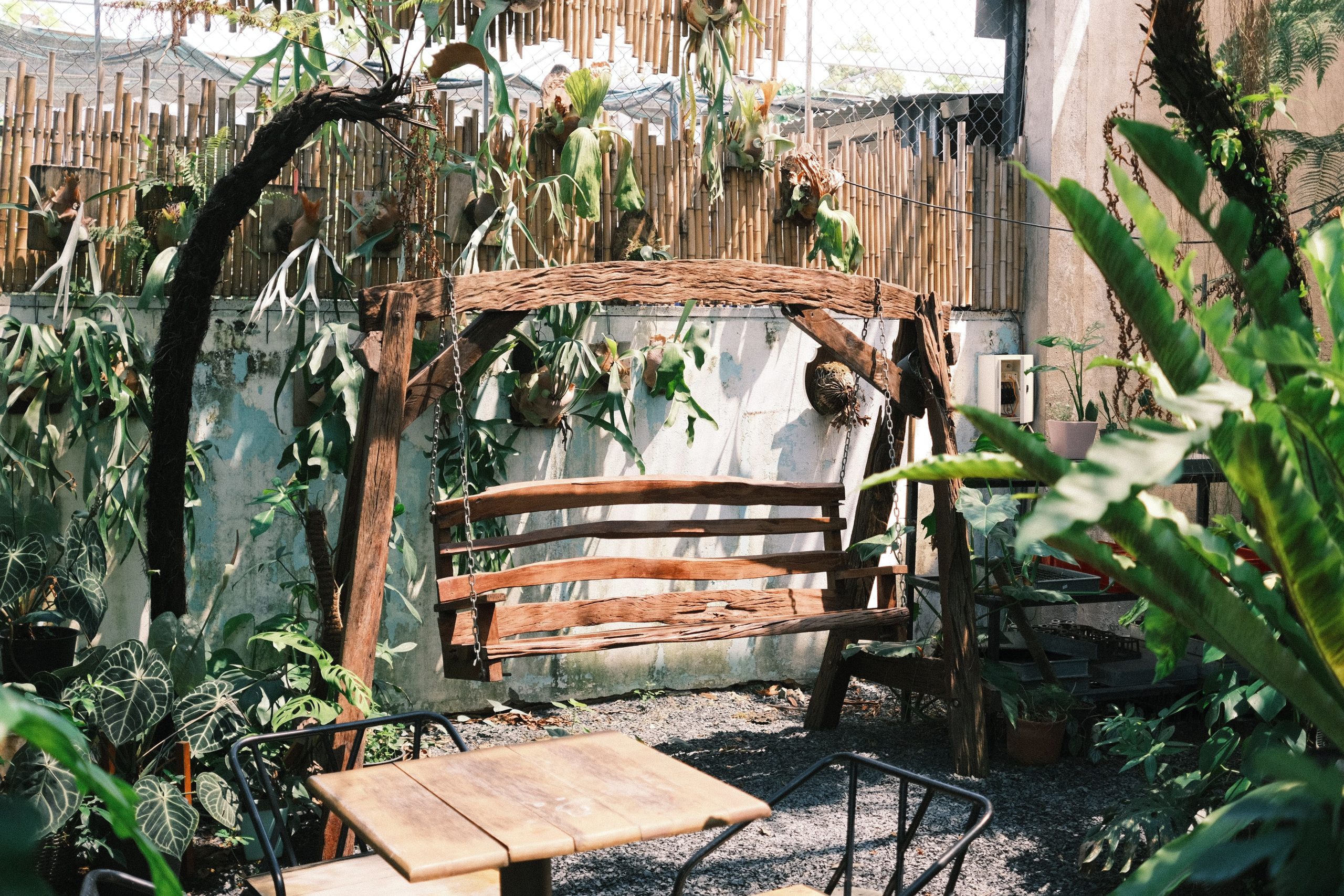 A serene rustic garden featuring a wooden swing, lush green foliage, and a tranquil setting.