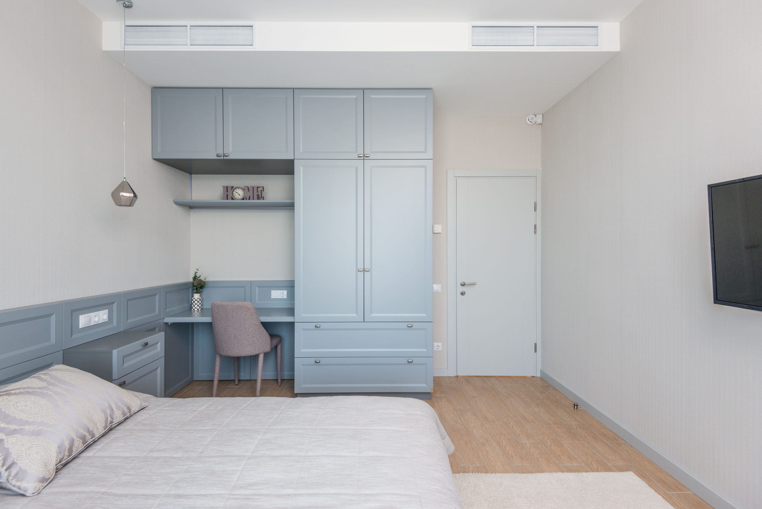 A sleek and modern bedroom with an integrated workspace featuring pastel blue cabinetry.
