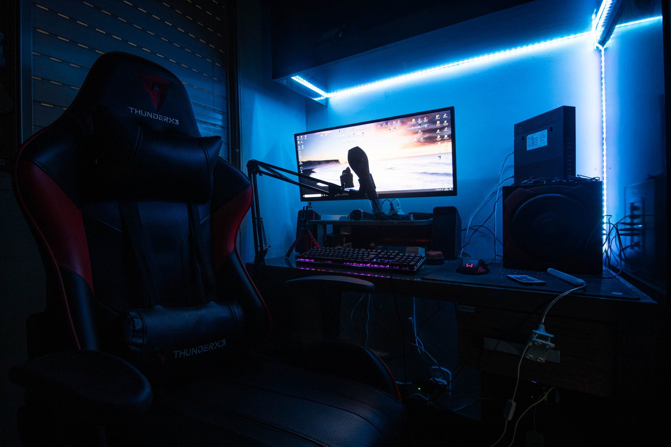 A sleek gaming desk with a monitor, gaming chair, and LED lights creating an immersive environment.