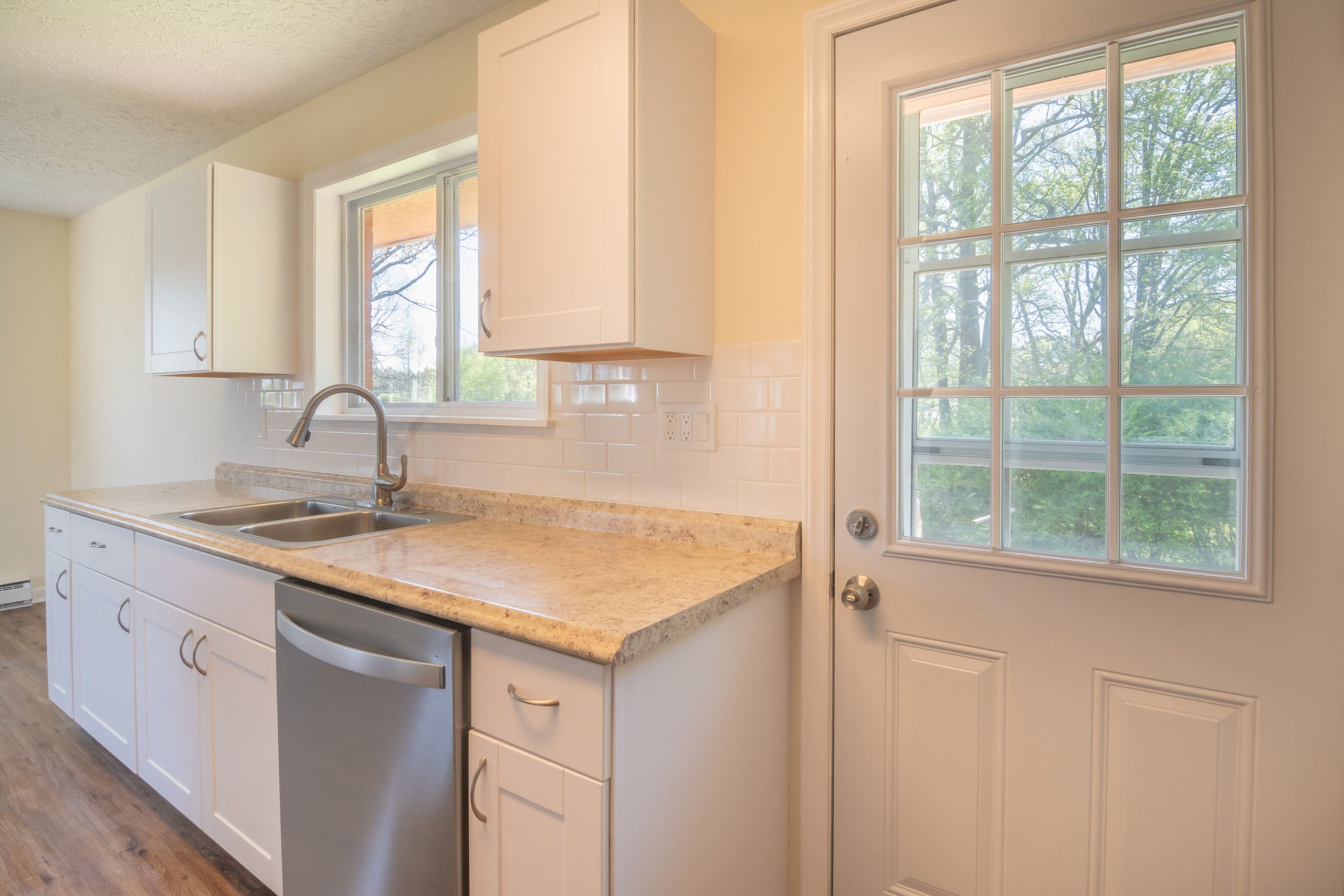 A sunlit modern kitchen with white cabinets, a sink, and a window view.