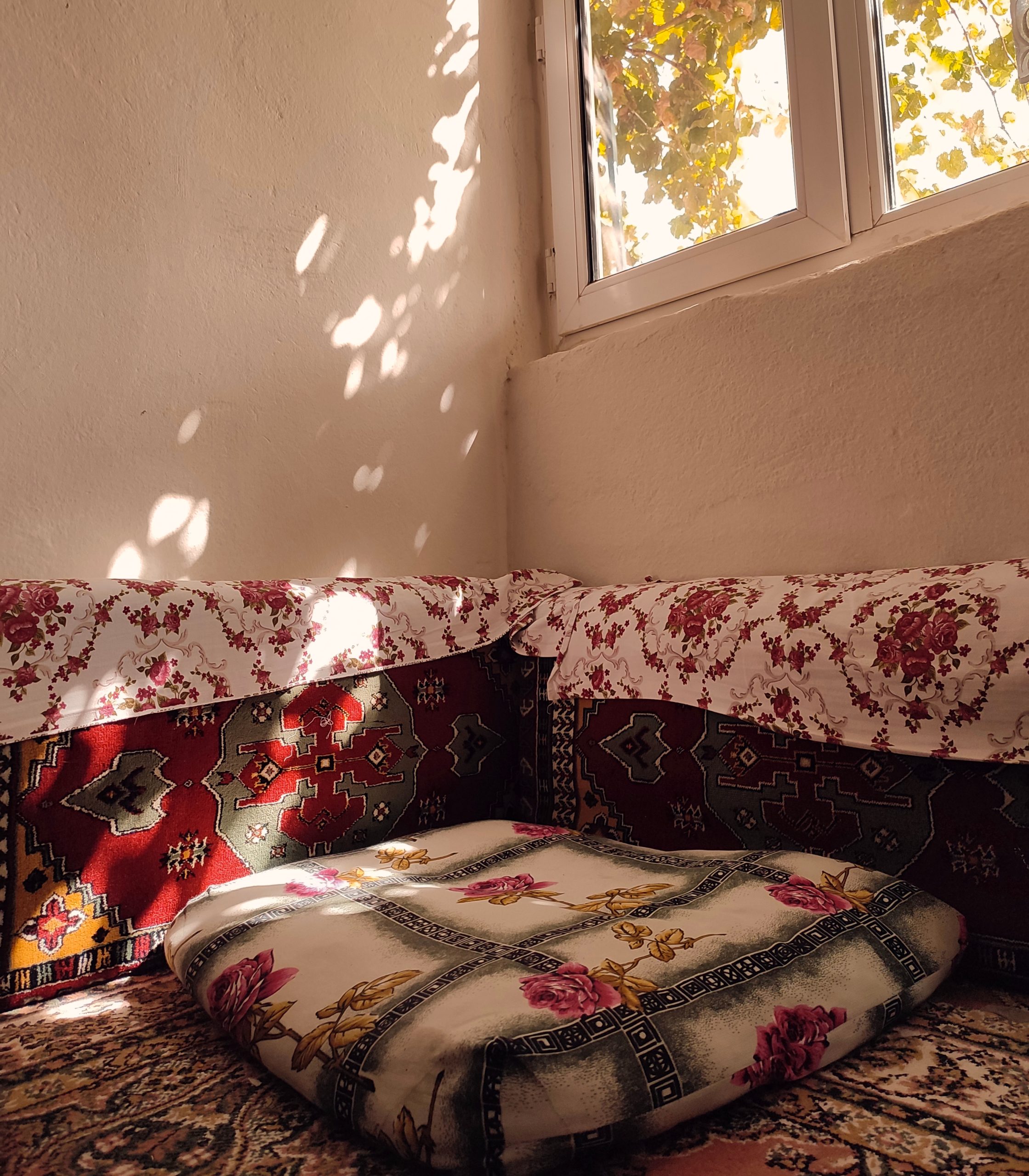 A sunlit room corner with vintage textiles and decorative pillows creating a cozy atmosphere.