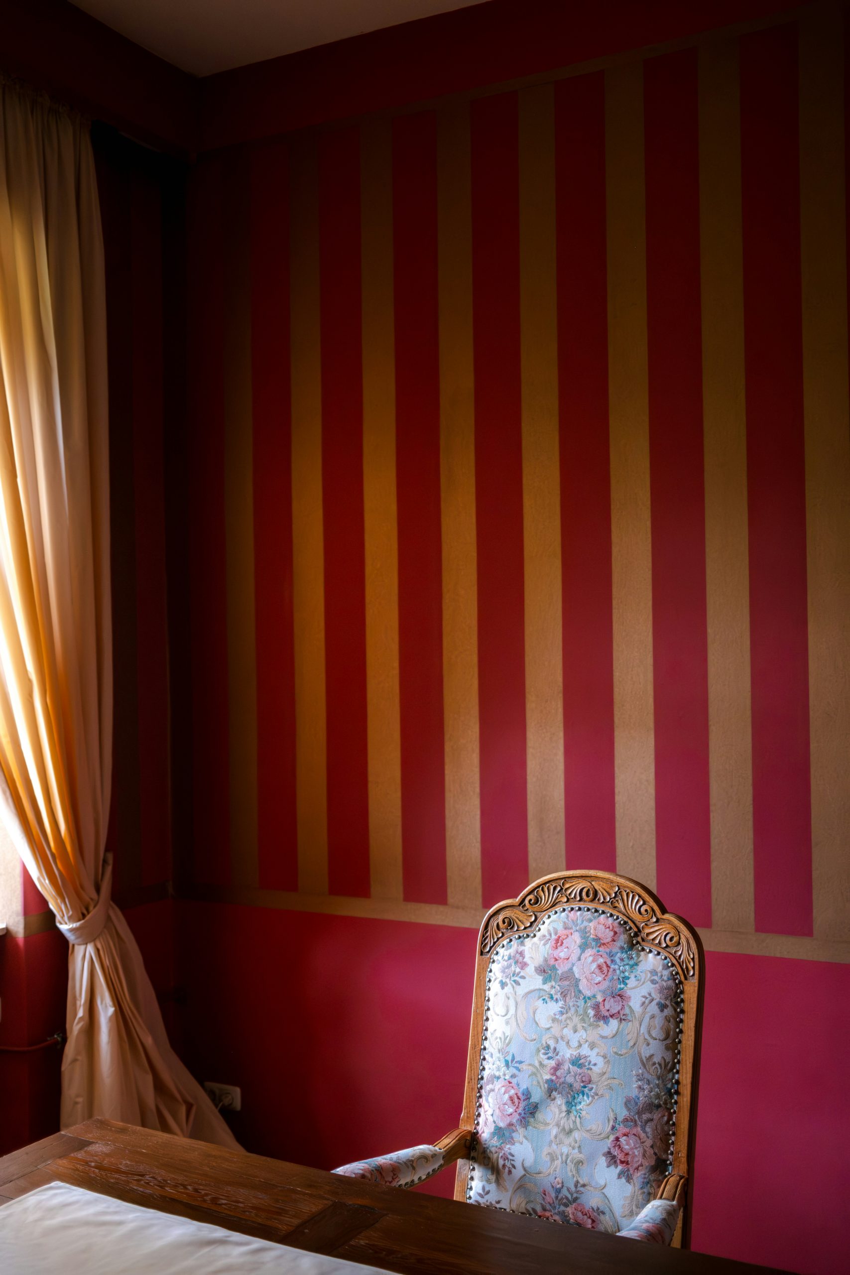 A vintage armchair with floral upholstery against striped walls.