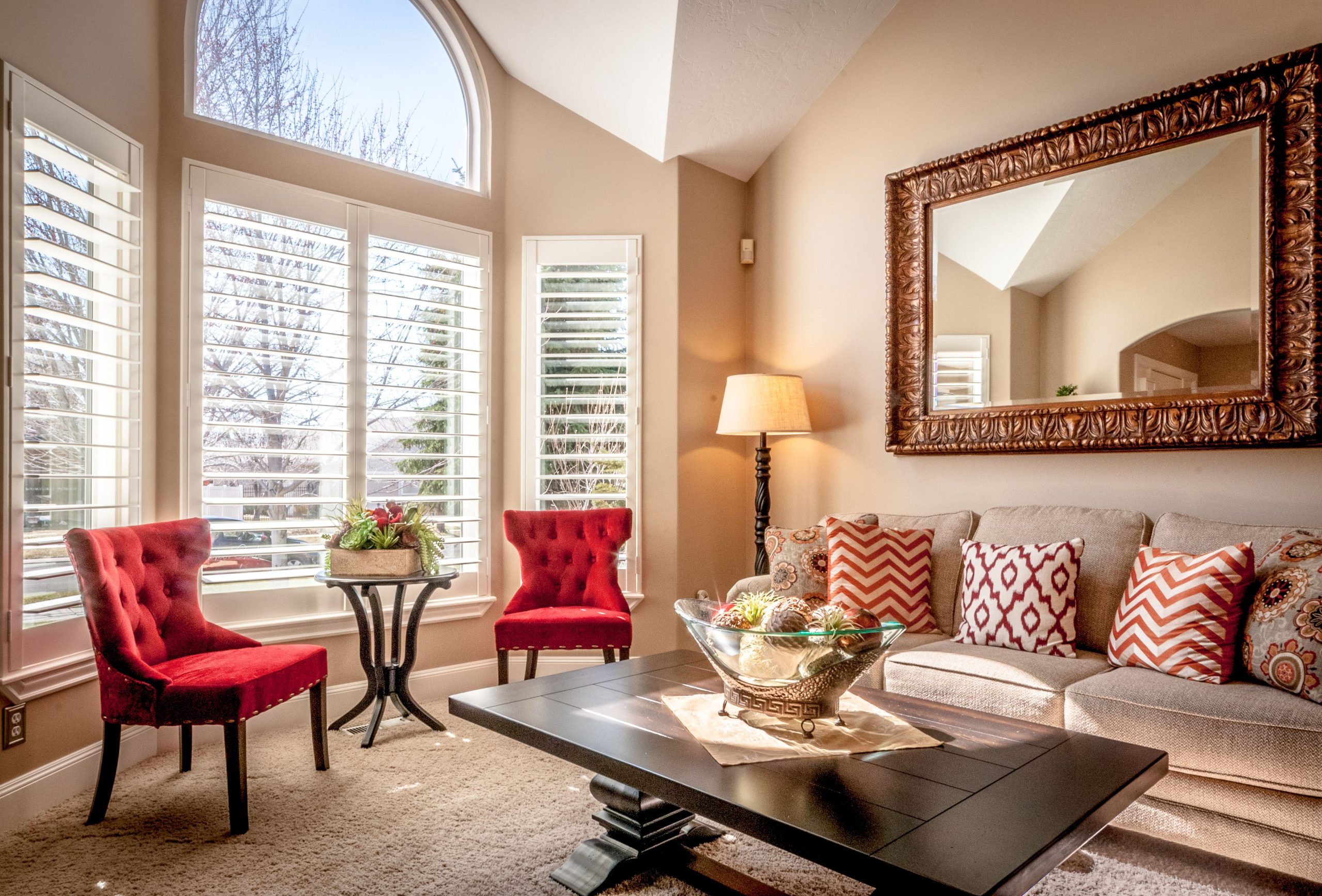 A warm and inviting living room with red chairs, patterned cushions, and a large arched window.