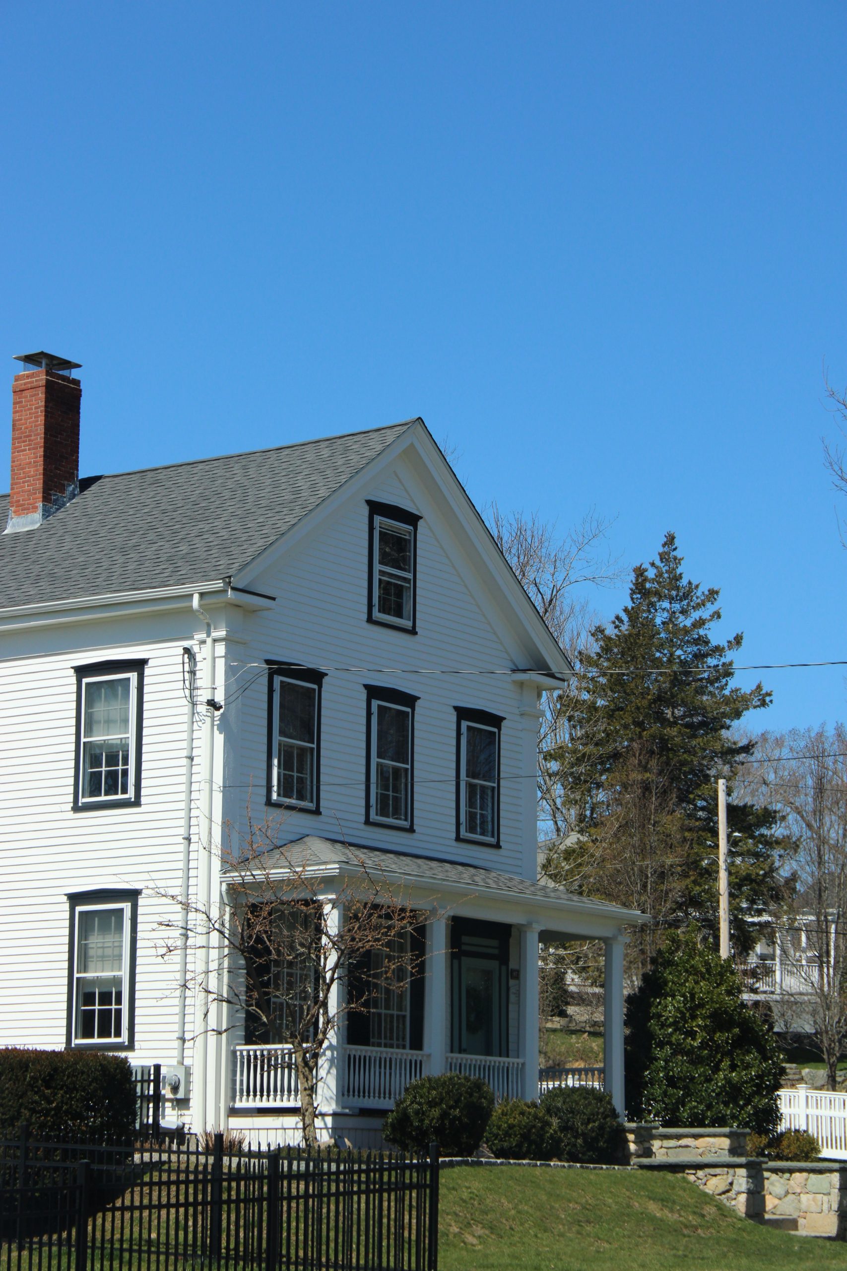A white colonial-style house in Massachusetts with a bright blue sky, showcasing timeless architecture.