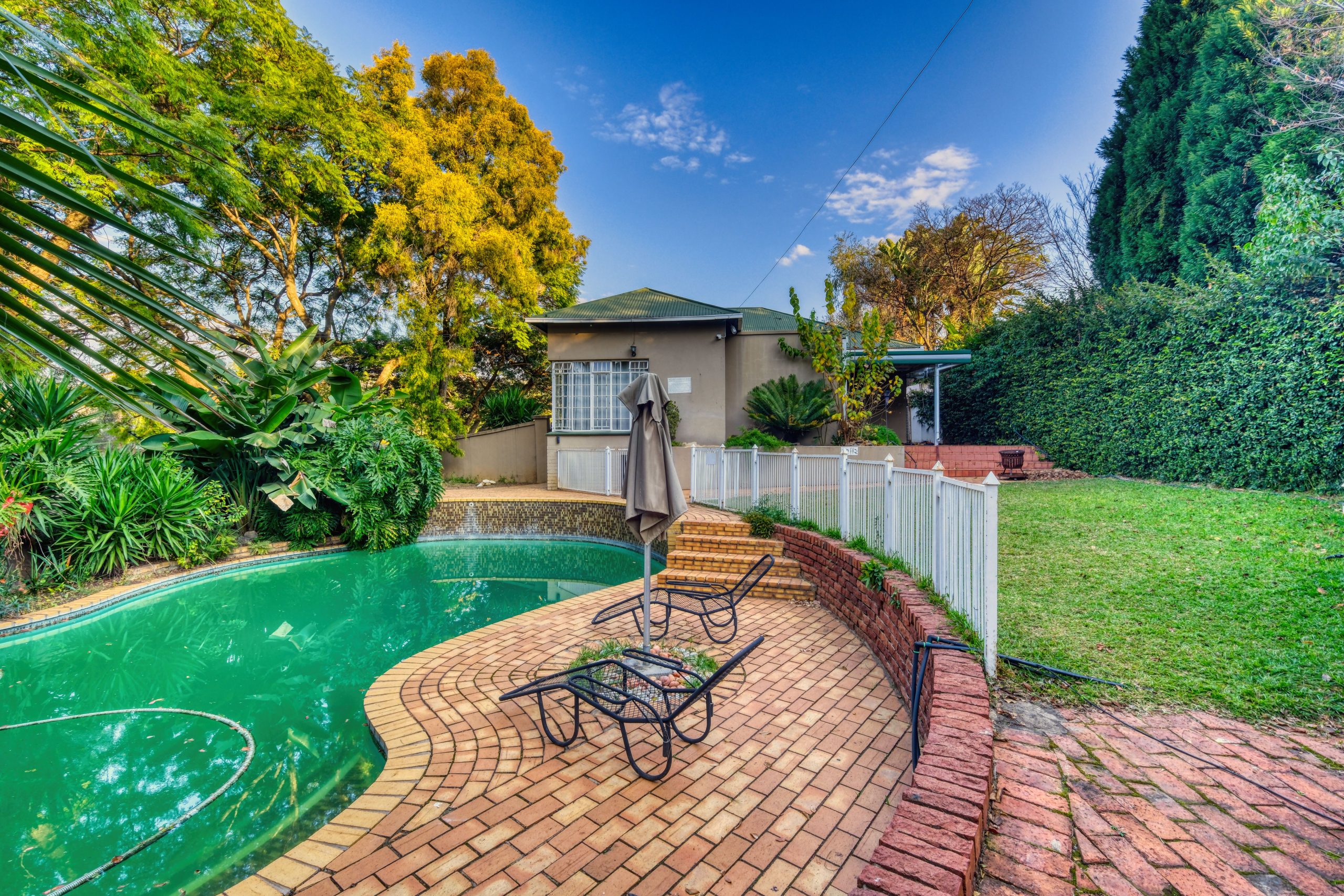 Beautiful backyard with brick patio, swimming pool, and lush garden in Pretoria, South Africa.