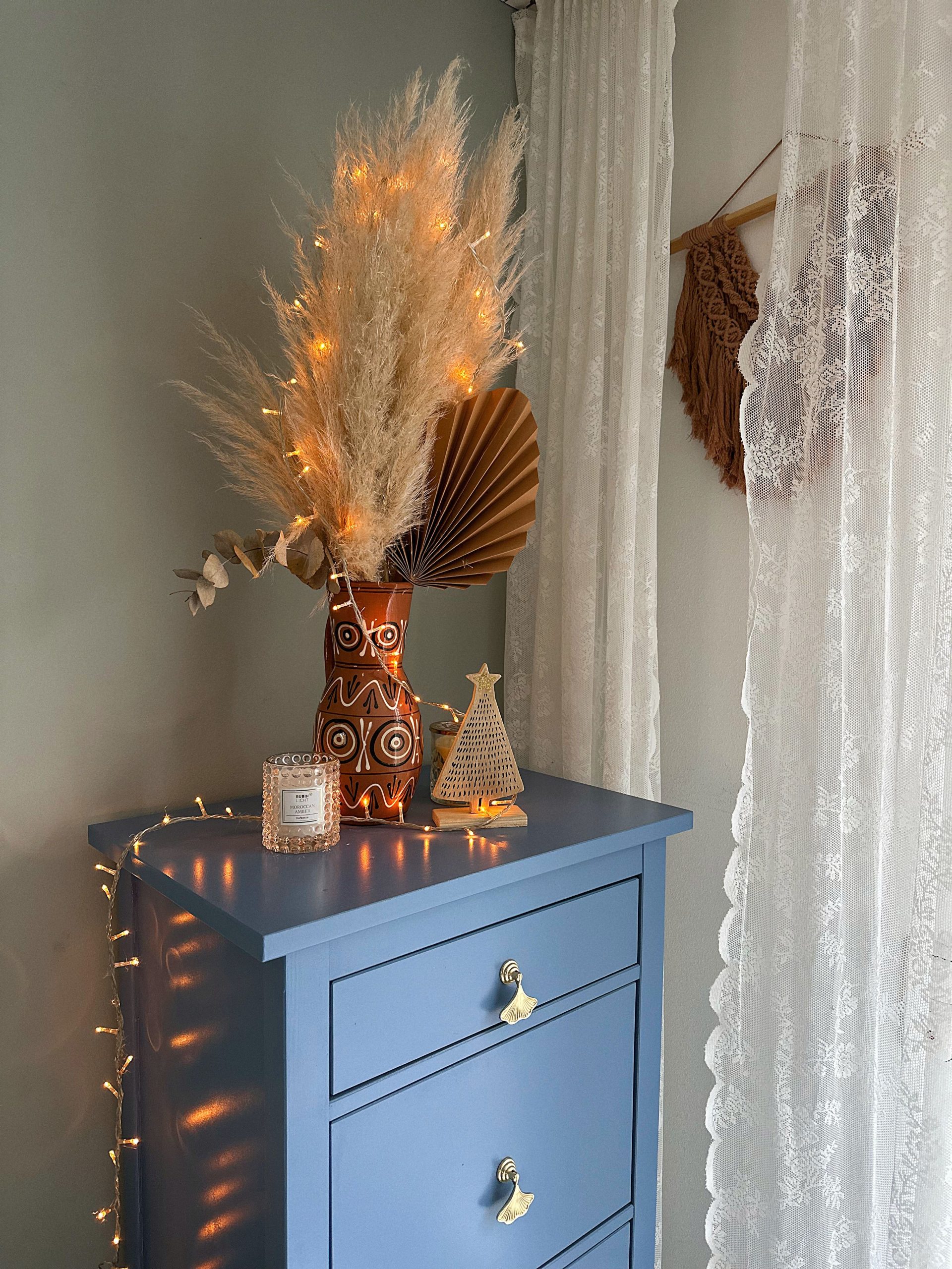 Boho-style corner with a blue dresser, pampas grass, and fairy lights, creating a warm atmosphere.