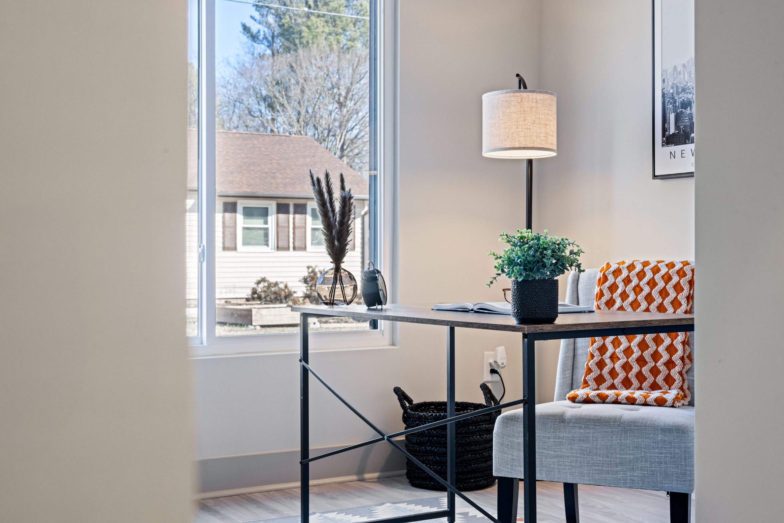 Bright modern home office with a minimalist desk, lamp, and cozy blanket by the window.