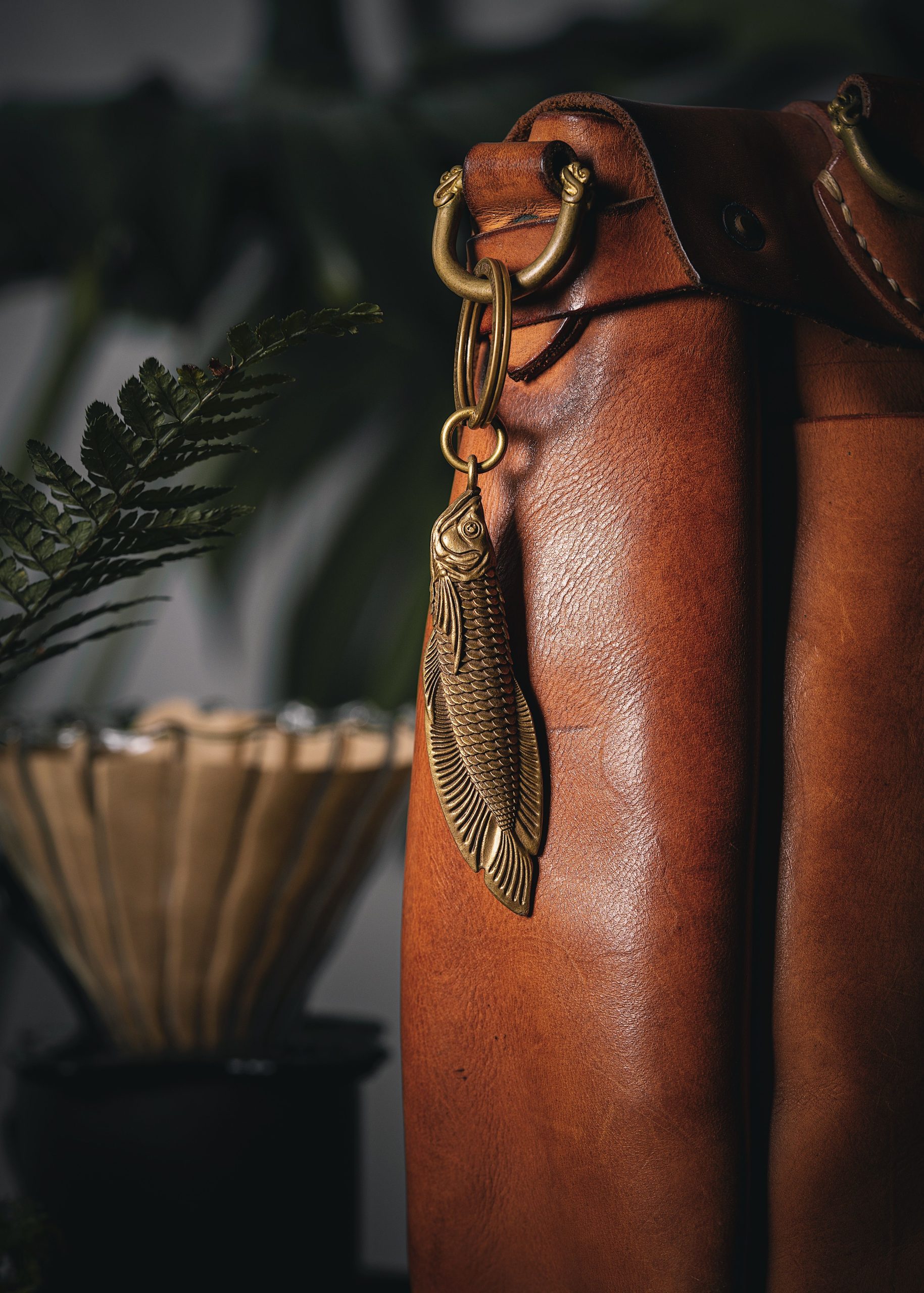 Close-up view of a leather bag featuring a fish-shaped metallic keychain.