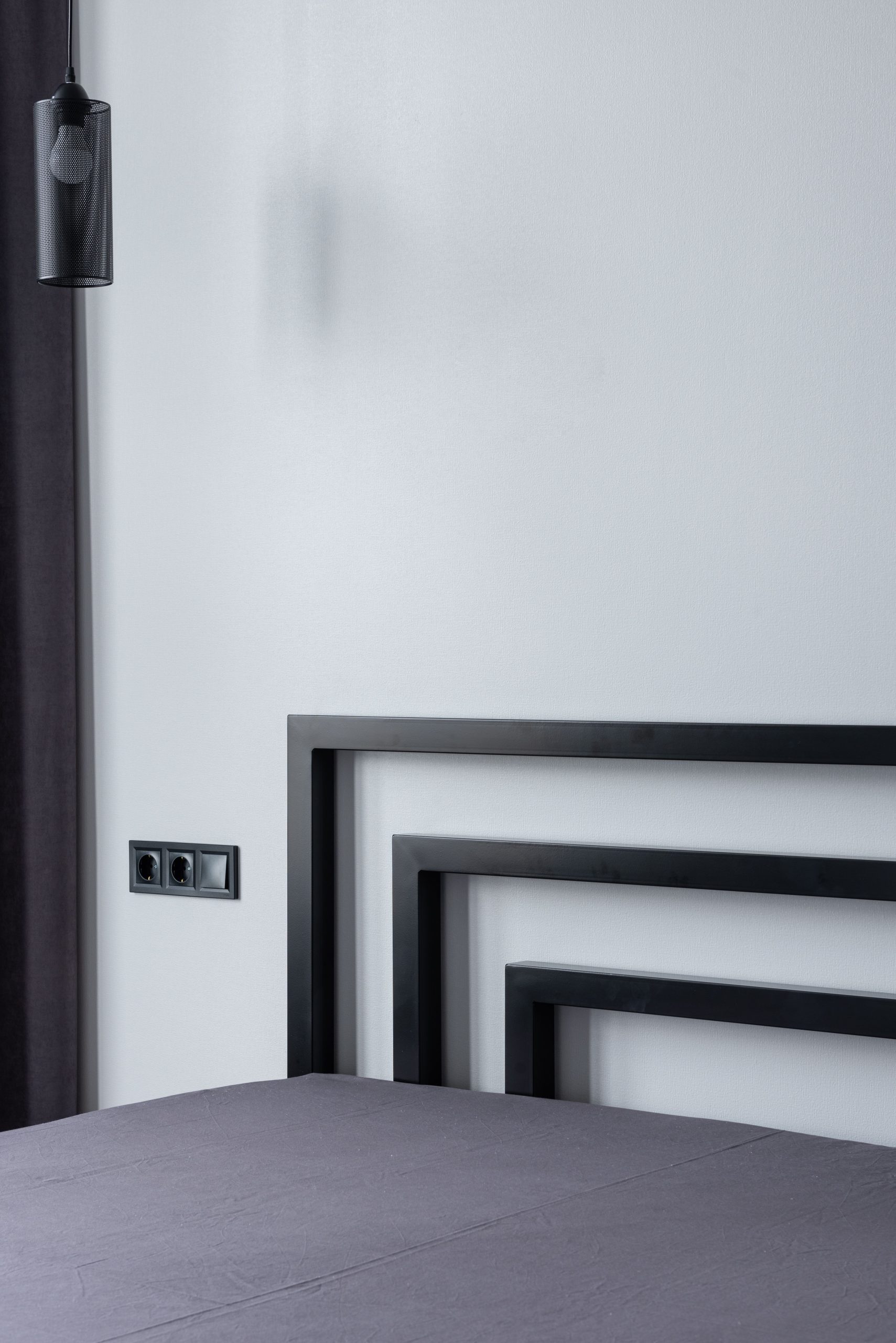 Contemporary bed with soft mattress against white wall with sockets and switch at home