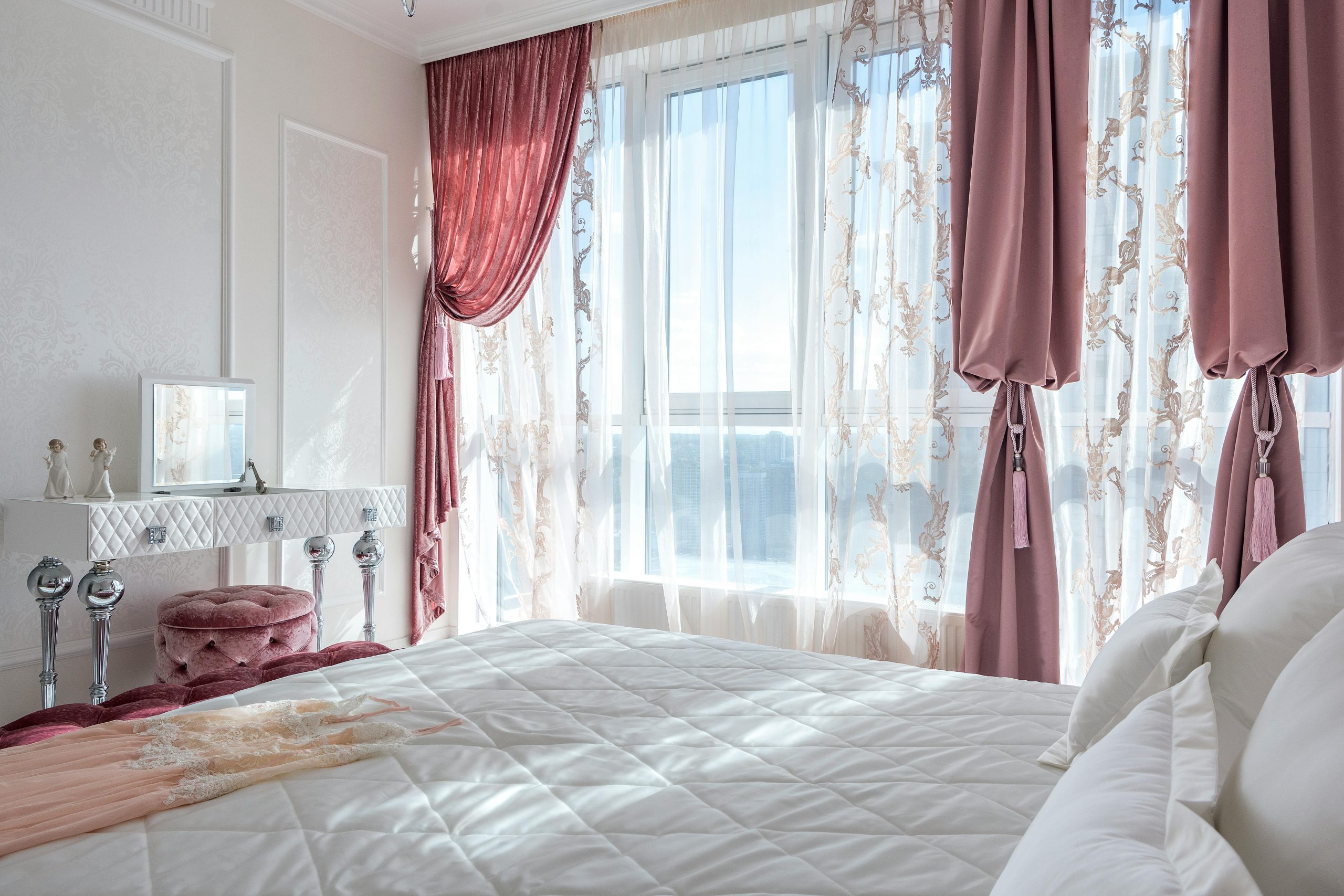 Cozy and elegant white and rosy bedroom with comfortable bed and draped curtains