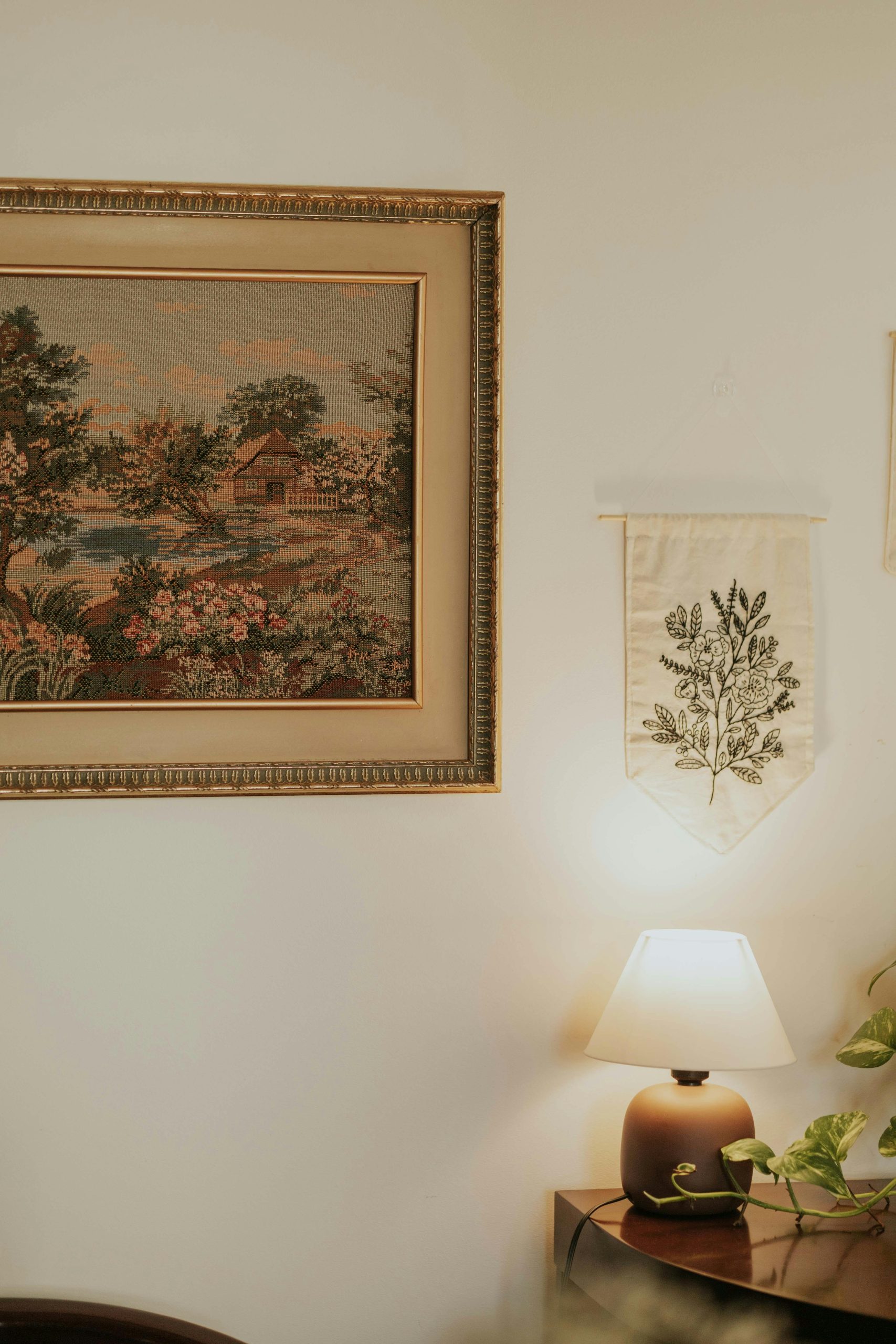 Cozy room decor featuring vintage art, a table lamp, and plants, creating a warm ambiance.