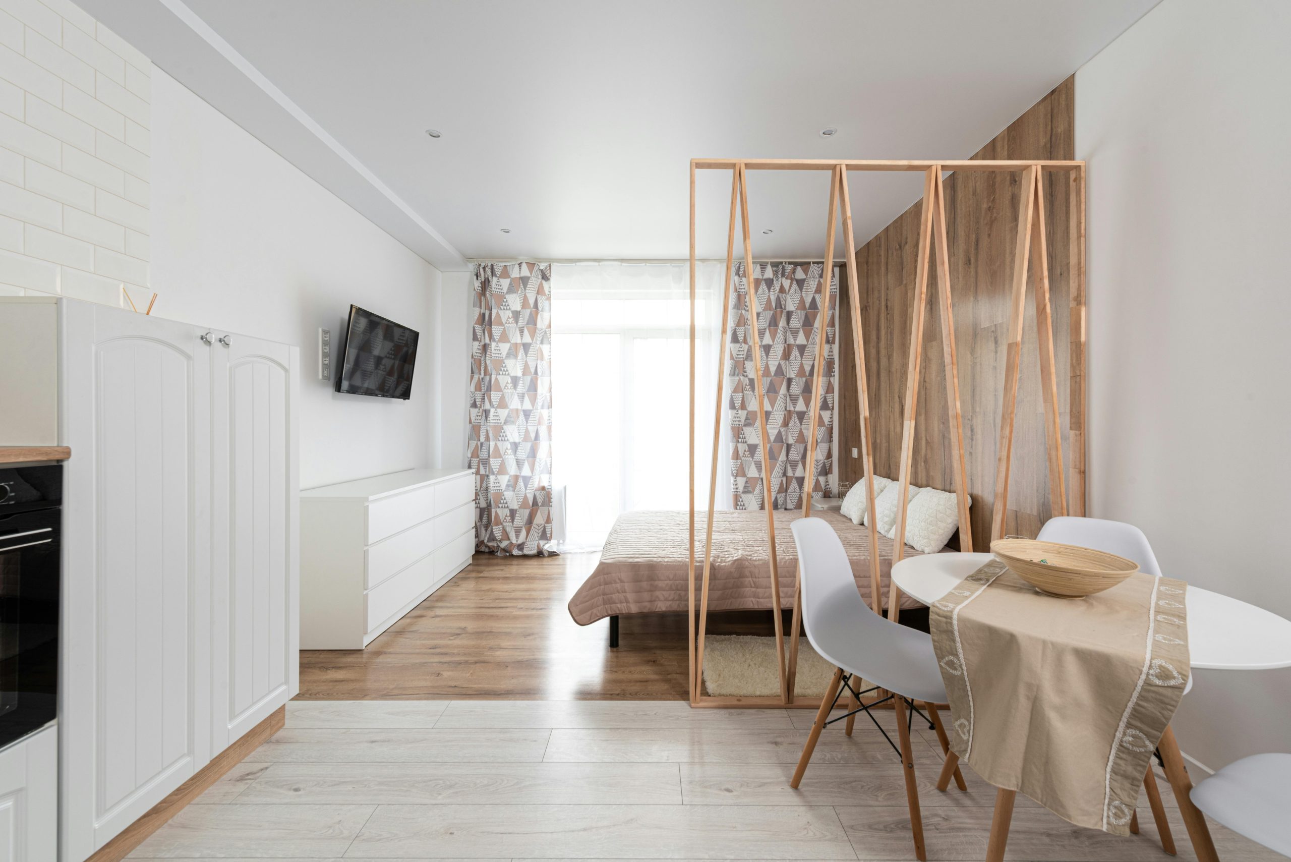 Creative design of dining room with table against bed and commode under television with black screen at home