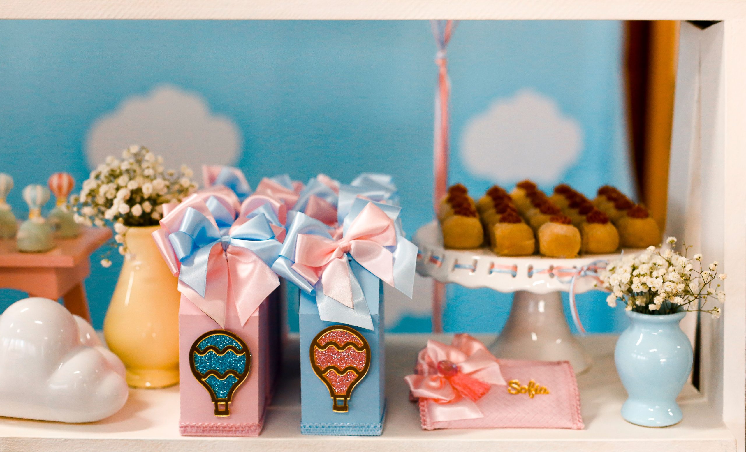 Delightful baby shower setup with pastel gift boxes, treats, and floral accent in a whimsical cloud setting.