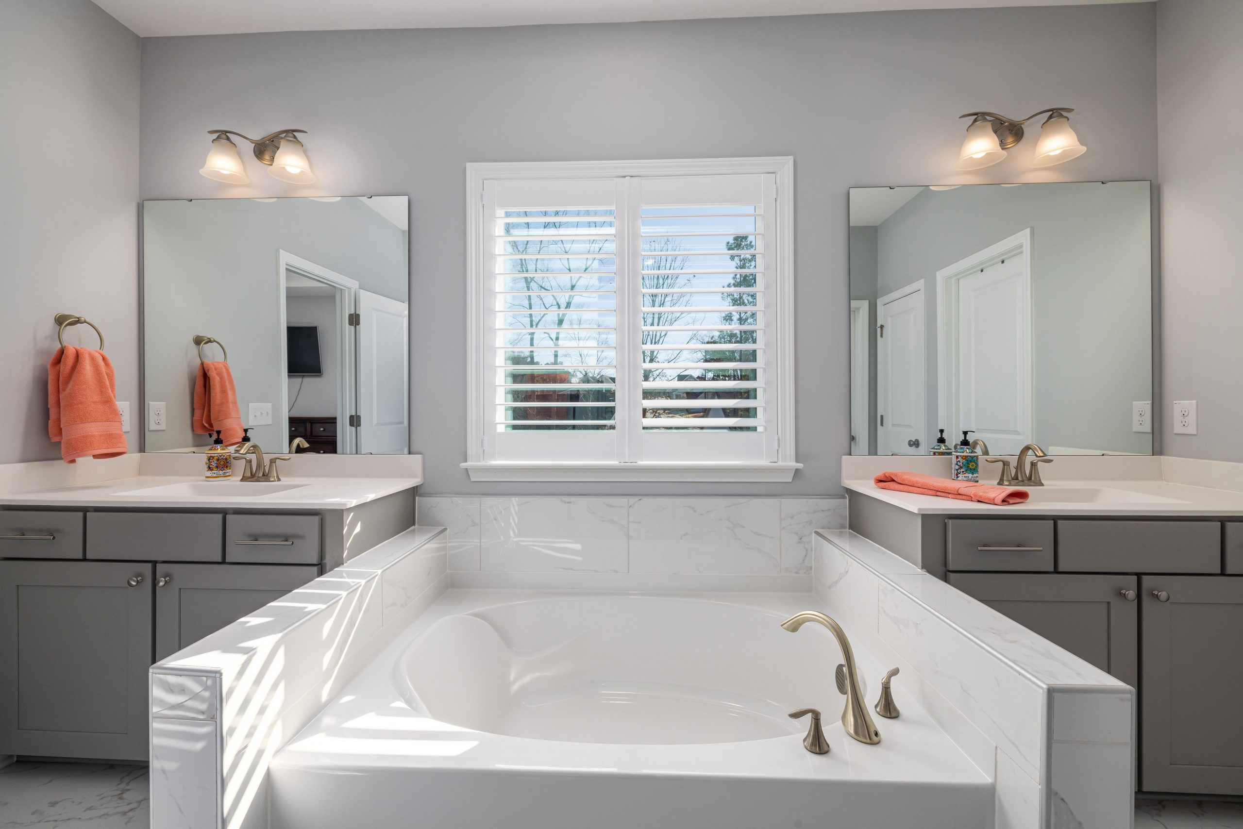 Elegant bathroom featuring a double vanity, bathtub, and natural light through window blinds.