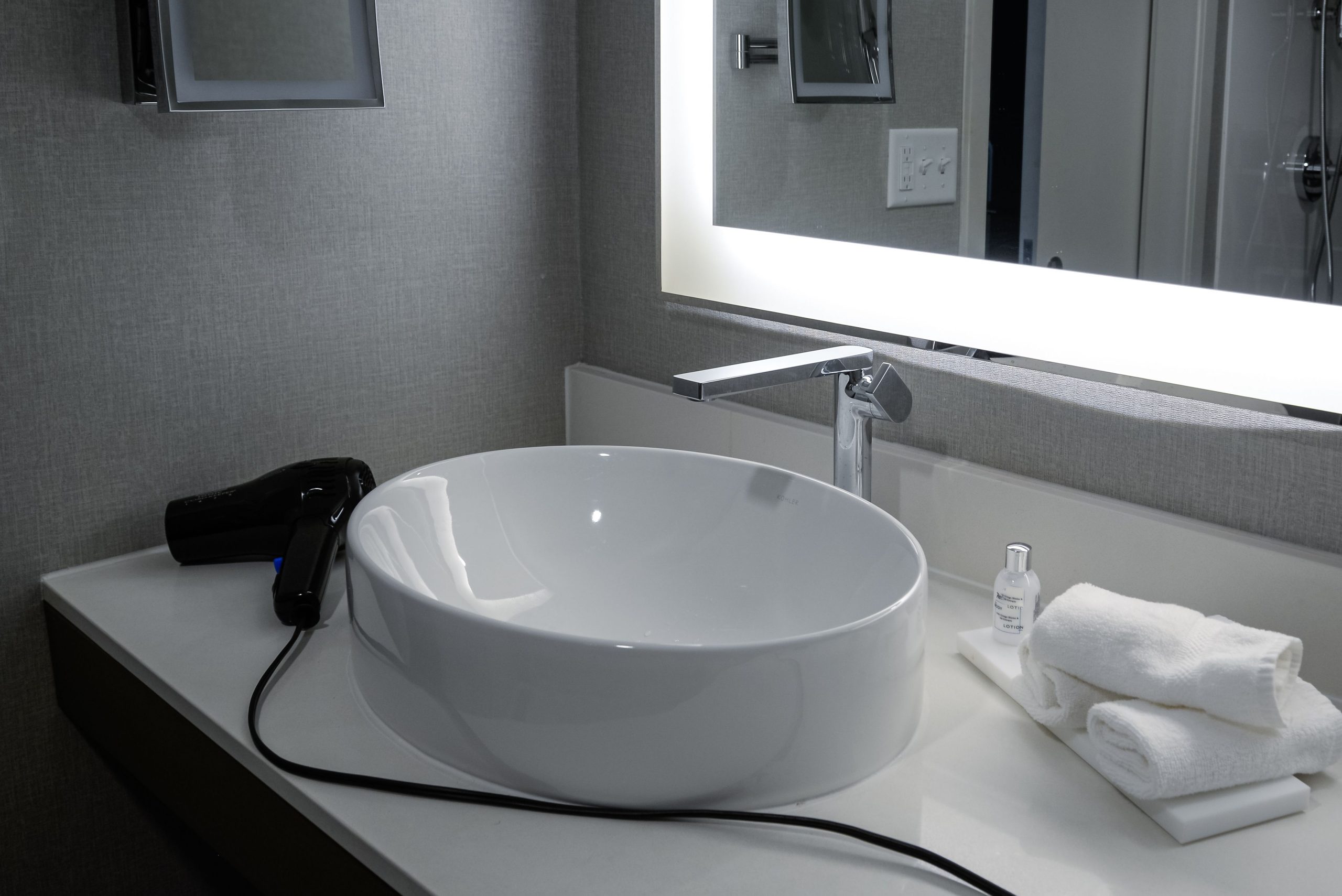 Elegant bathroom vanity with bowl sink, lighted mirror, and hairdryer in a hotel setting.